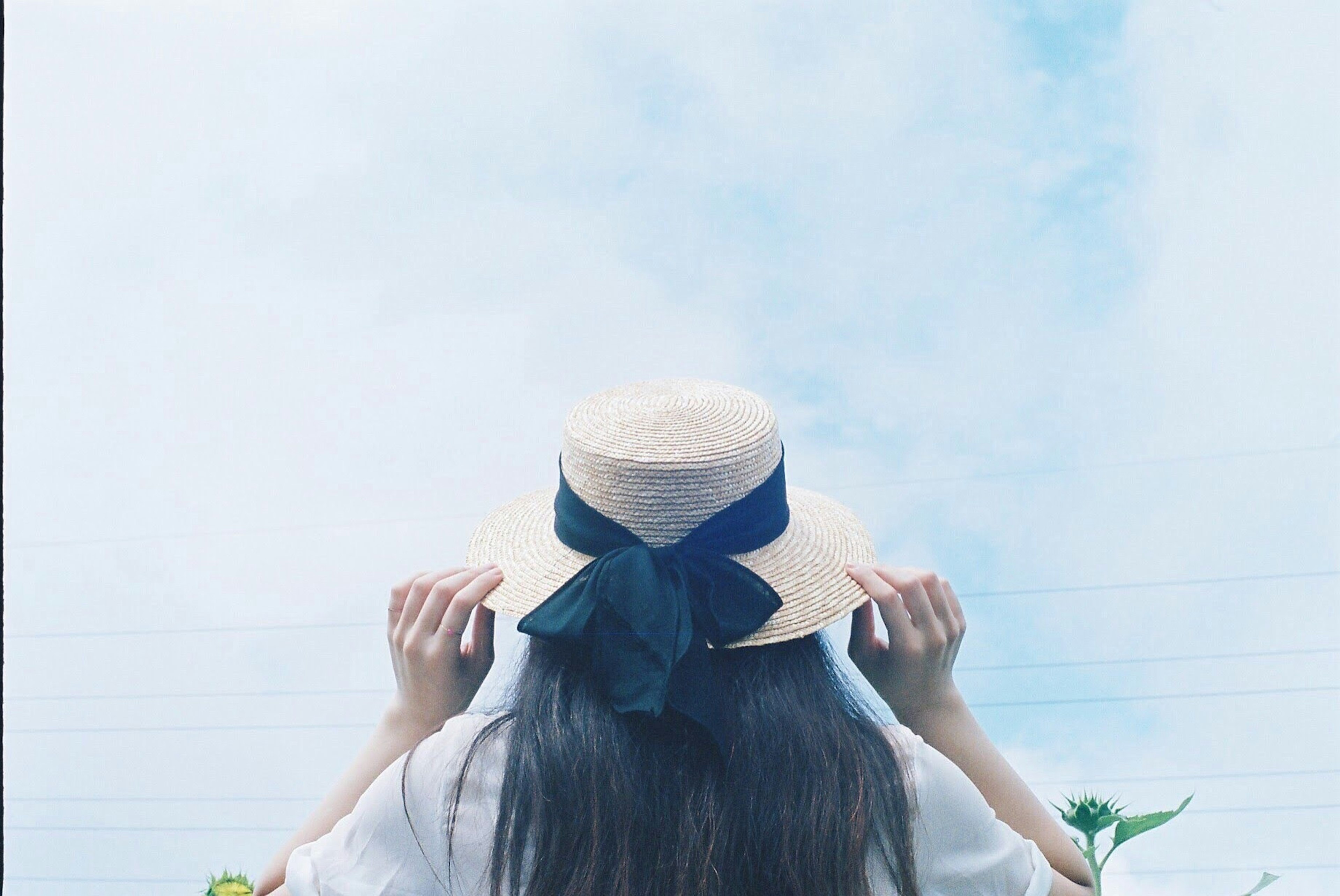 Mujer sosteniendo un sombrero bajo un cielo azul