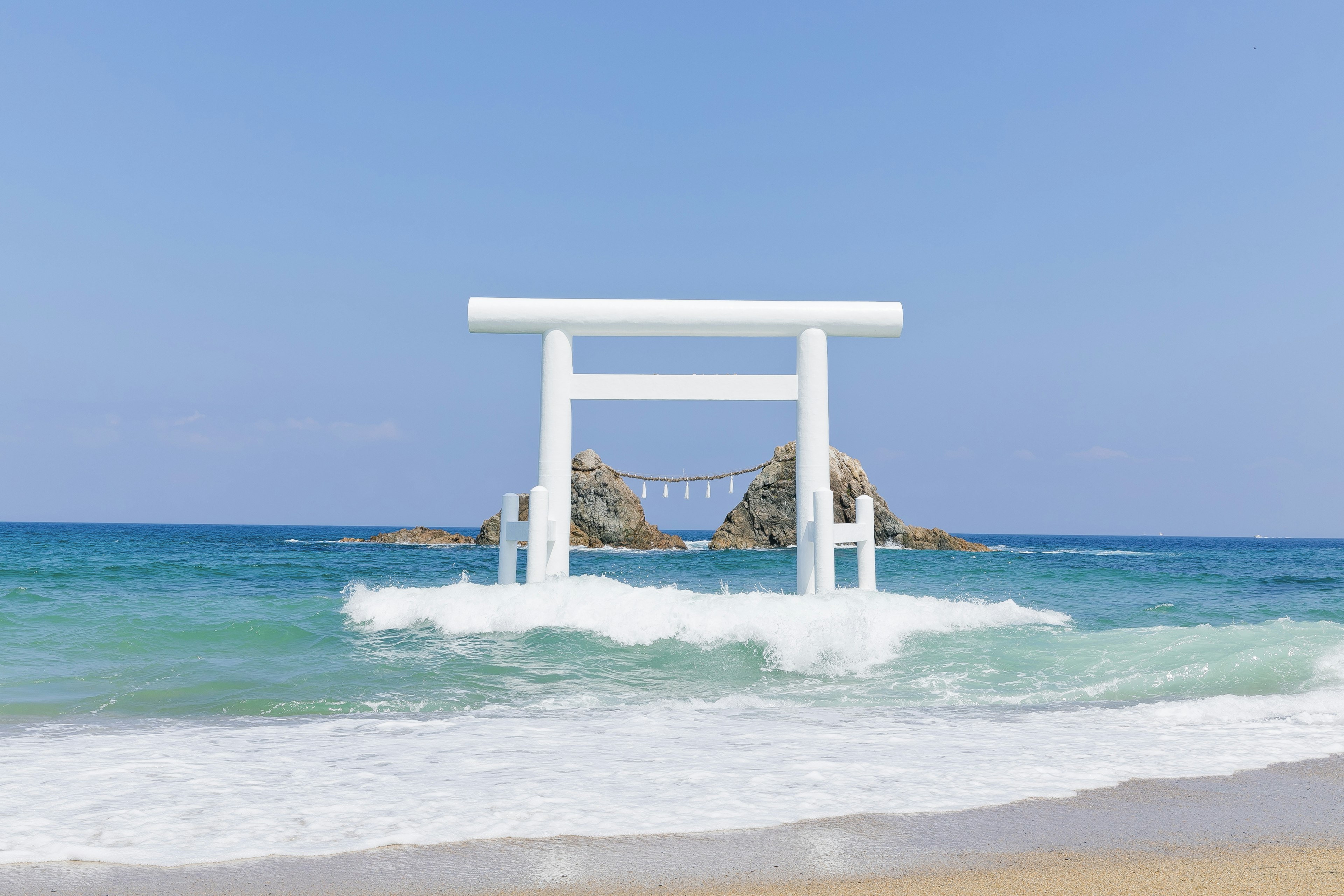 White torii gate in the ocean with rocks under a blue sky