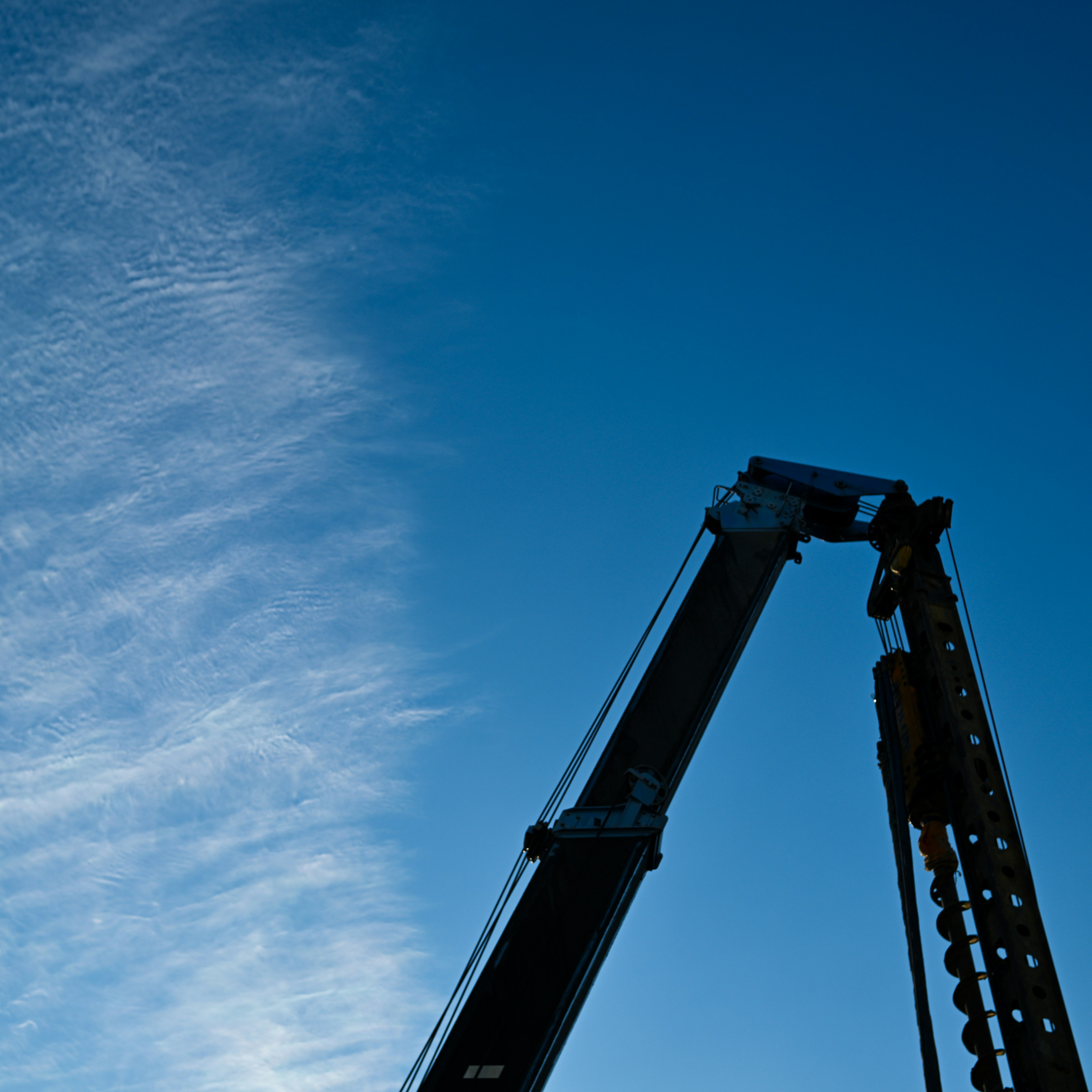 Silhouette of a crane against a blue sky with wispy clouds