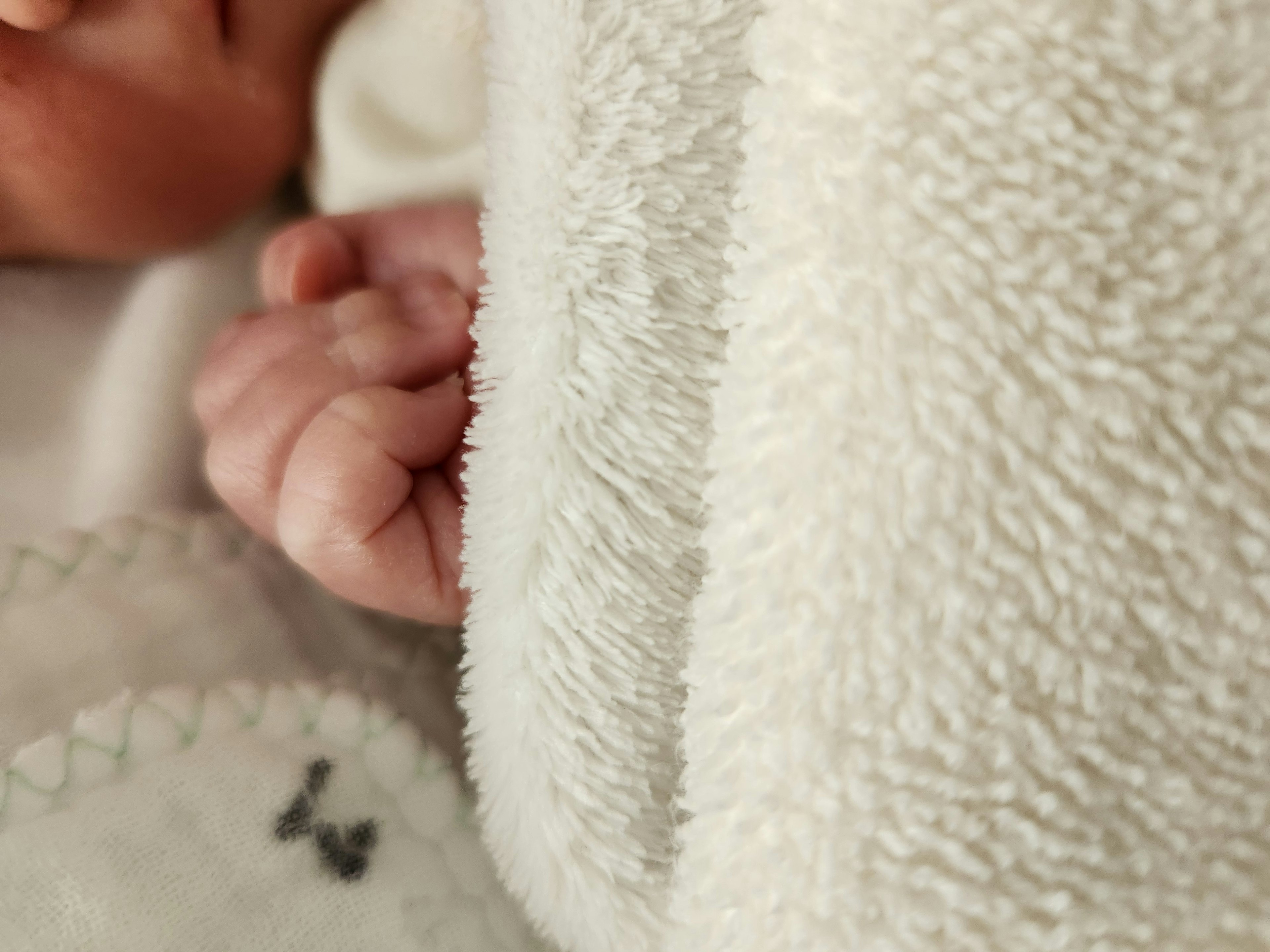 A close-up of a baby's small hand peeking from under a soft blanket