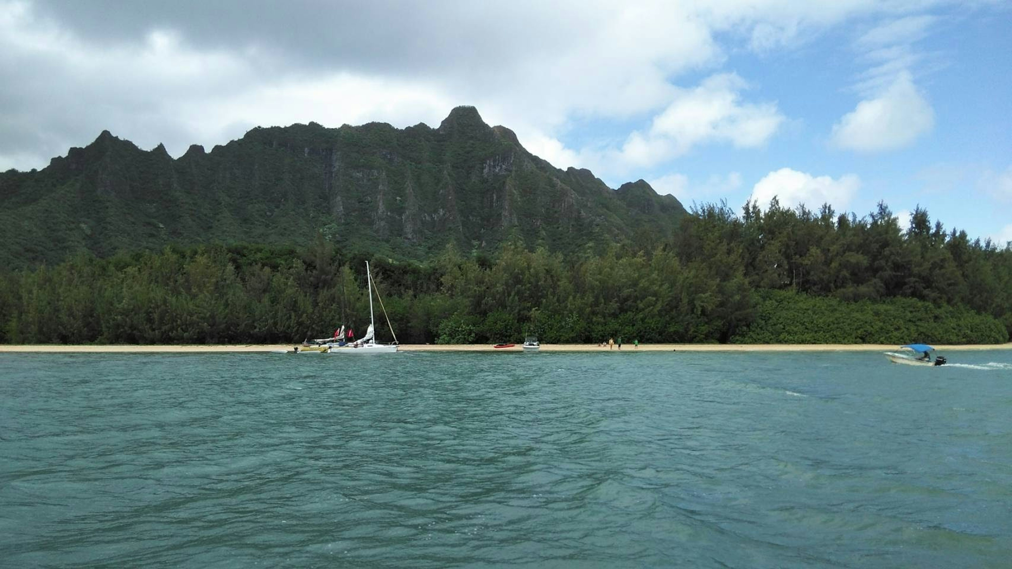 Une vue pittoresque avec un voilier près d'une plage de sable et des montagnes verdoyantes en arrière-plan