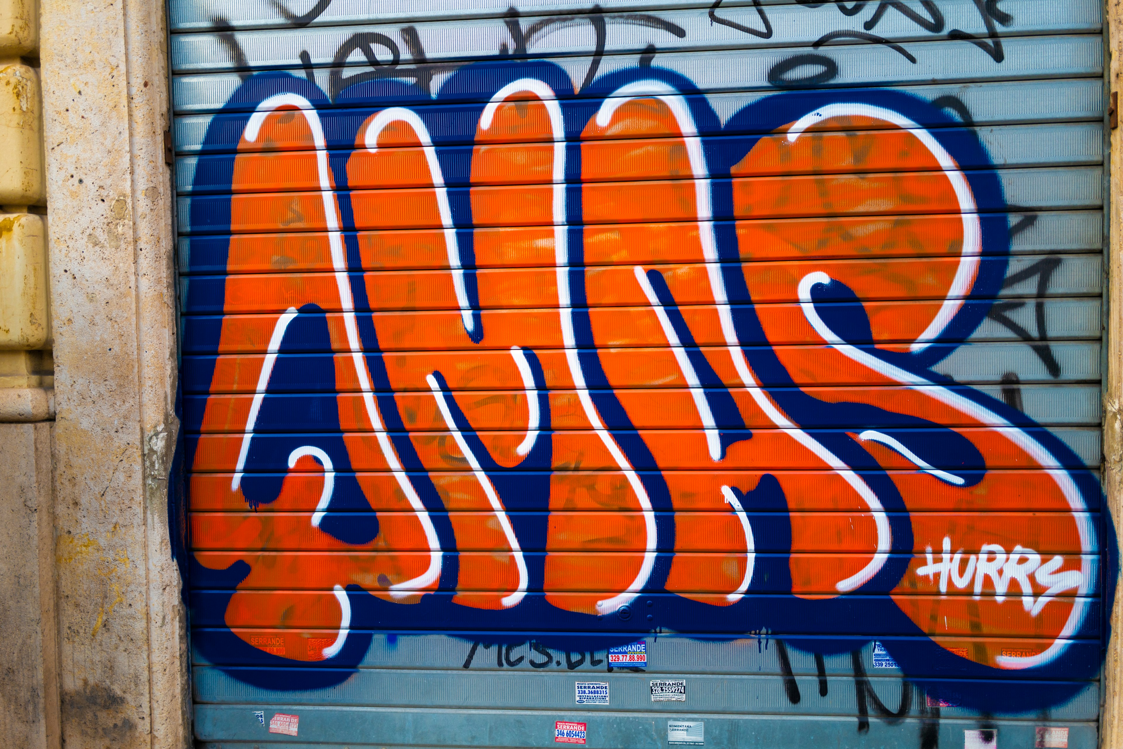 Orange graffiti on a blue shutter featuring bold lettering with a unique style