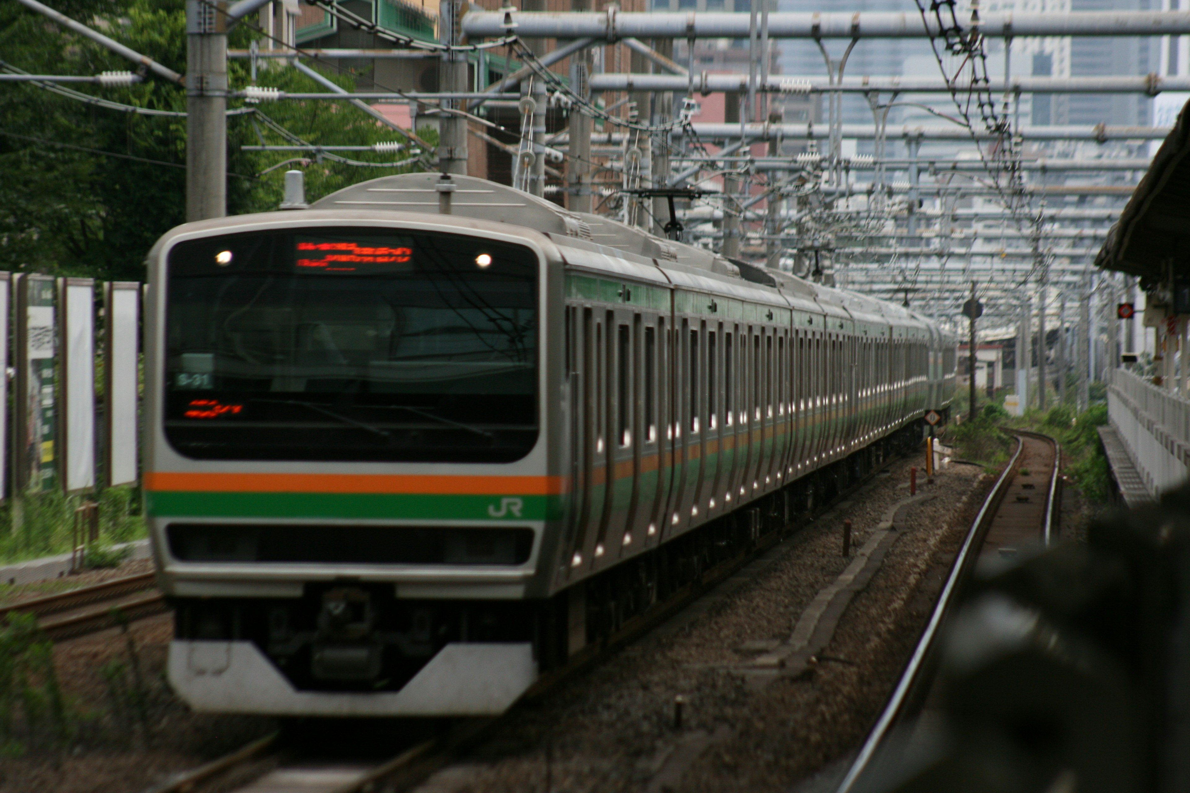 Train de banlieue japonais avec des rayures vertes et orange circulant sur les rails