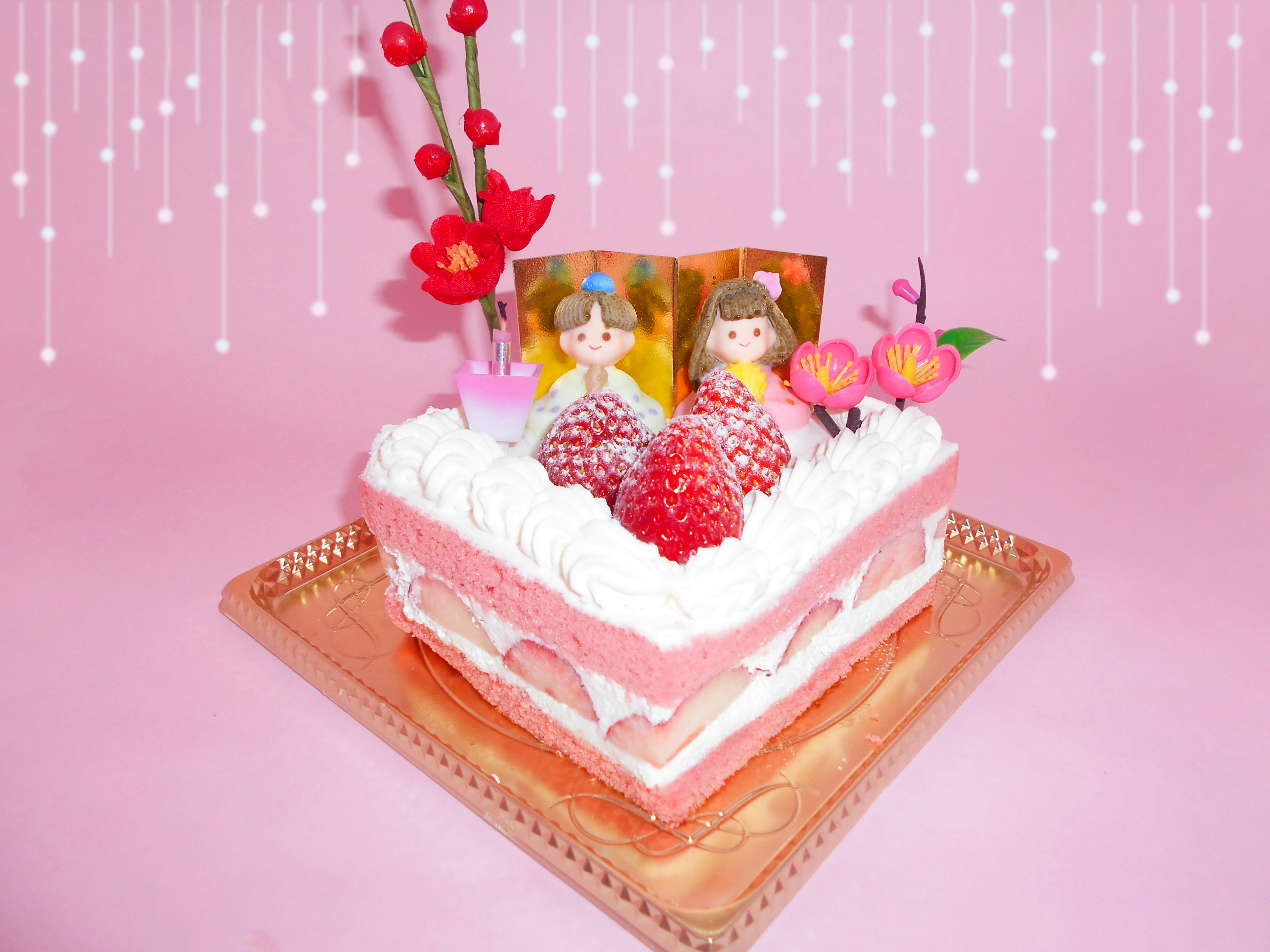 A heart-shaped cake decorated with strawberries and flowers set against a pink background