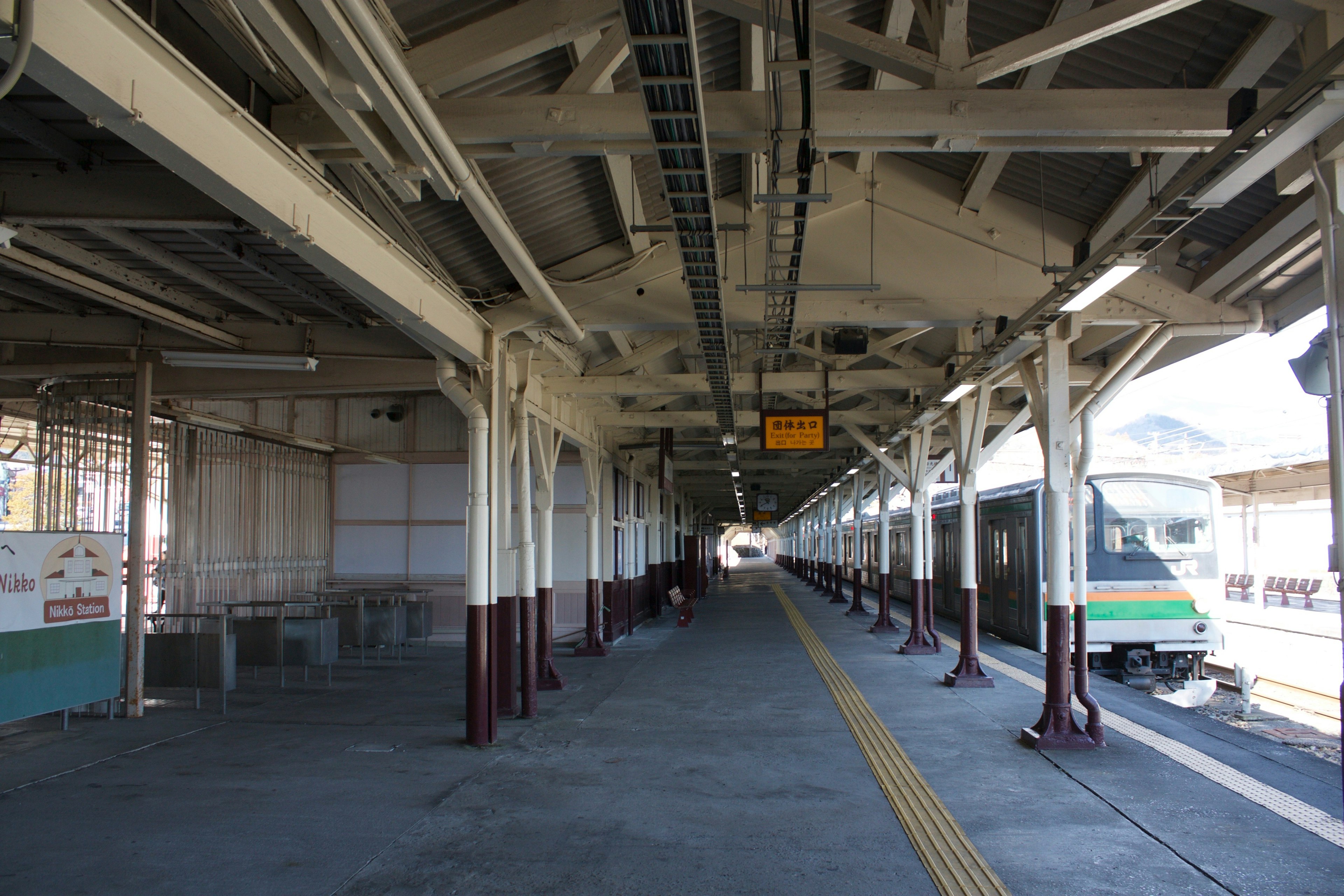 Vista interior de una plataforma de estación de tren con elementos estructurales y un tren visible