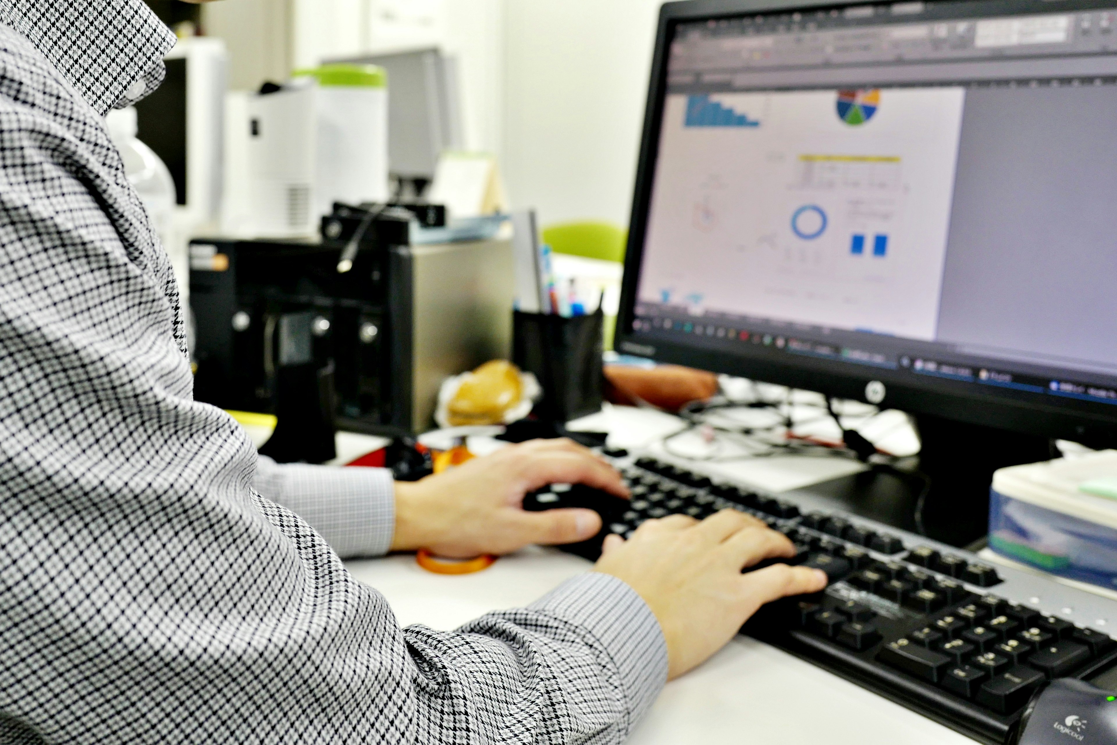 A man's hand on a keyboard working on a computer displaying graphs and designs