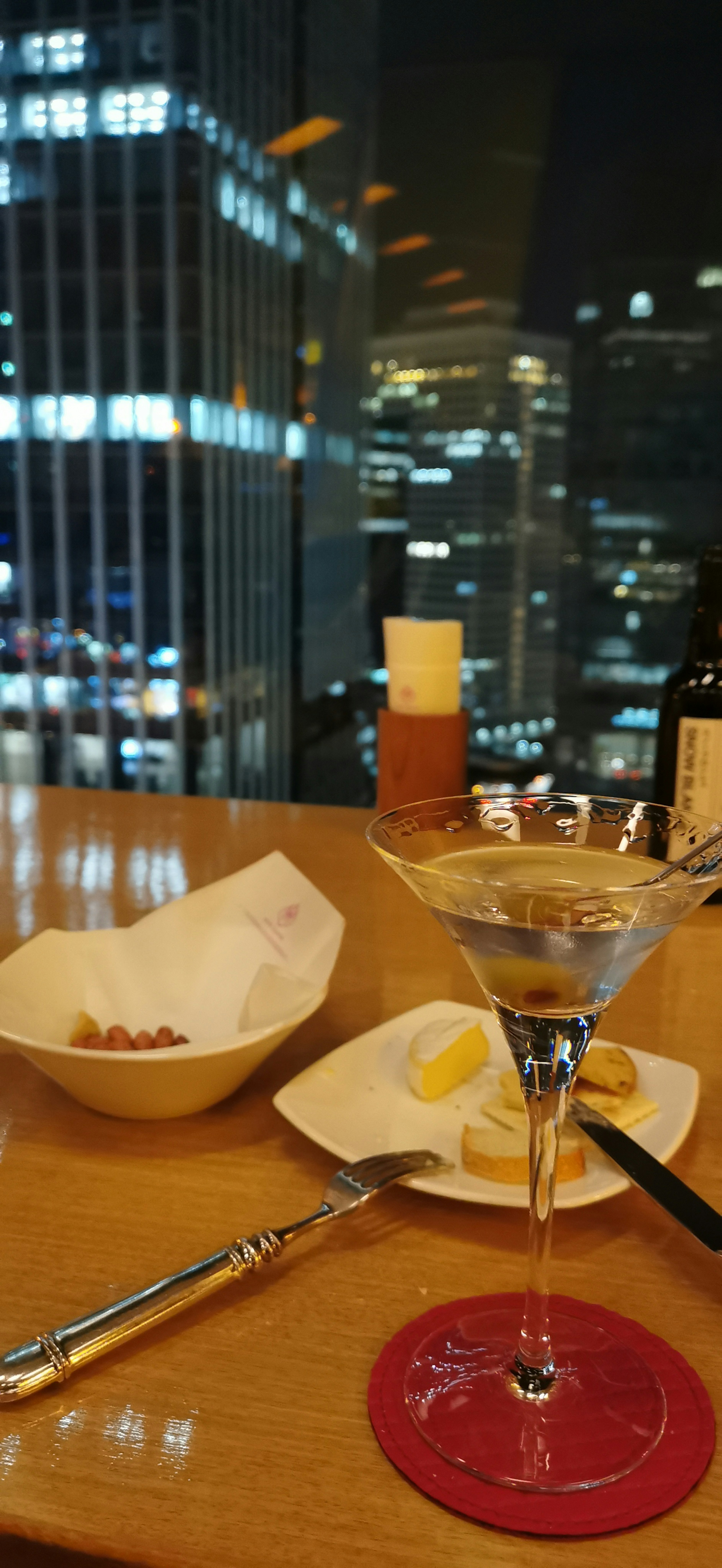 Cocktail glass with snacks against a backdrop of city skyline at night