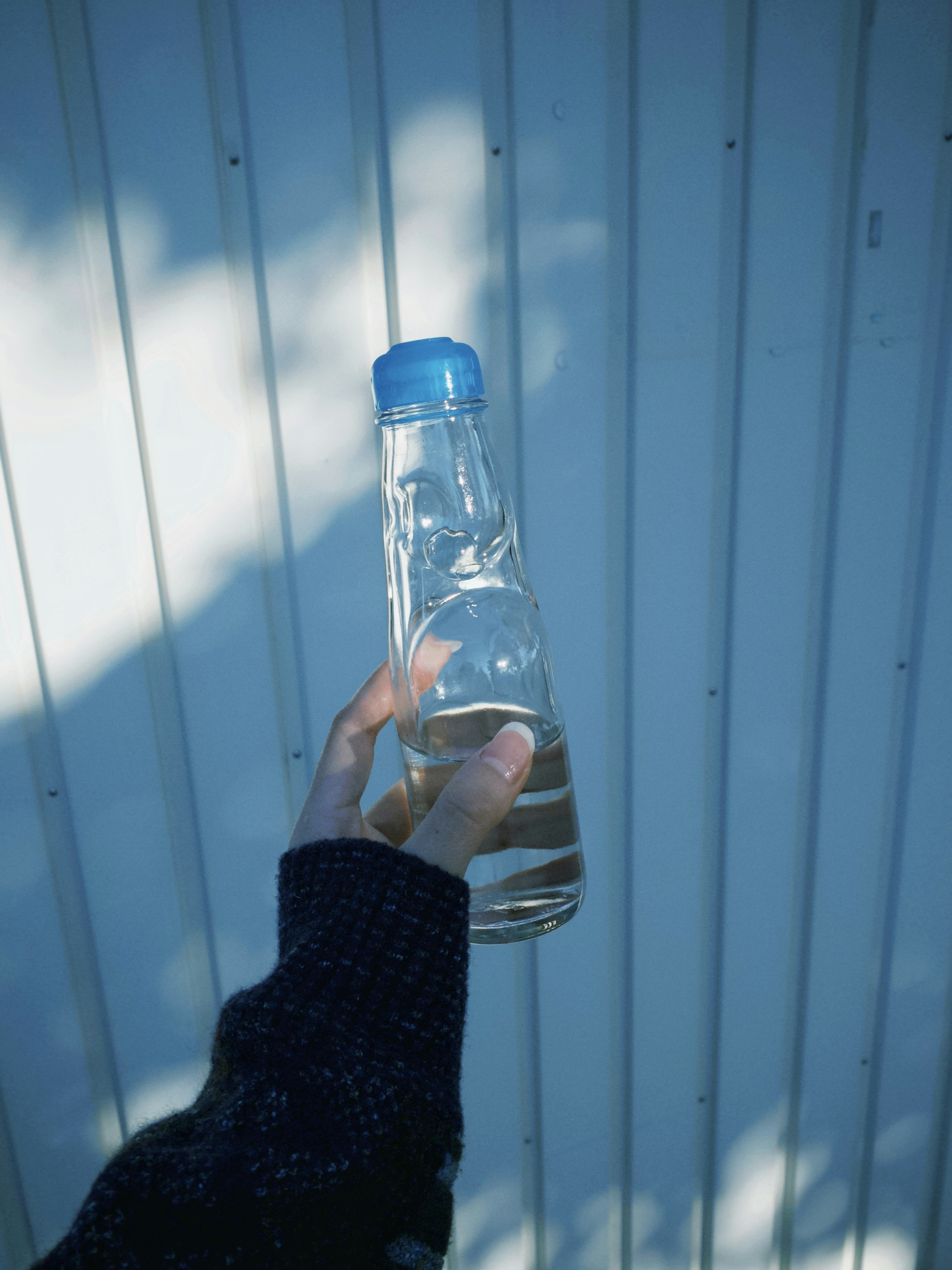 A hand holding a clear bottle of water with a blue cap