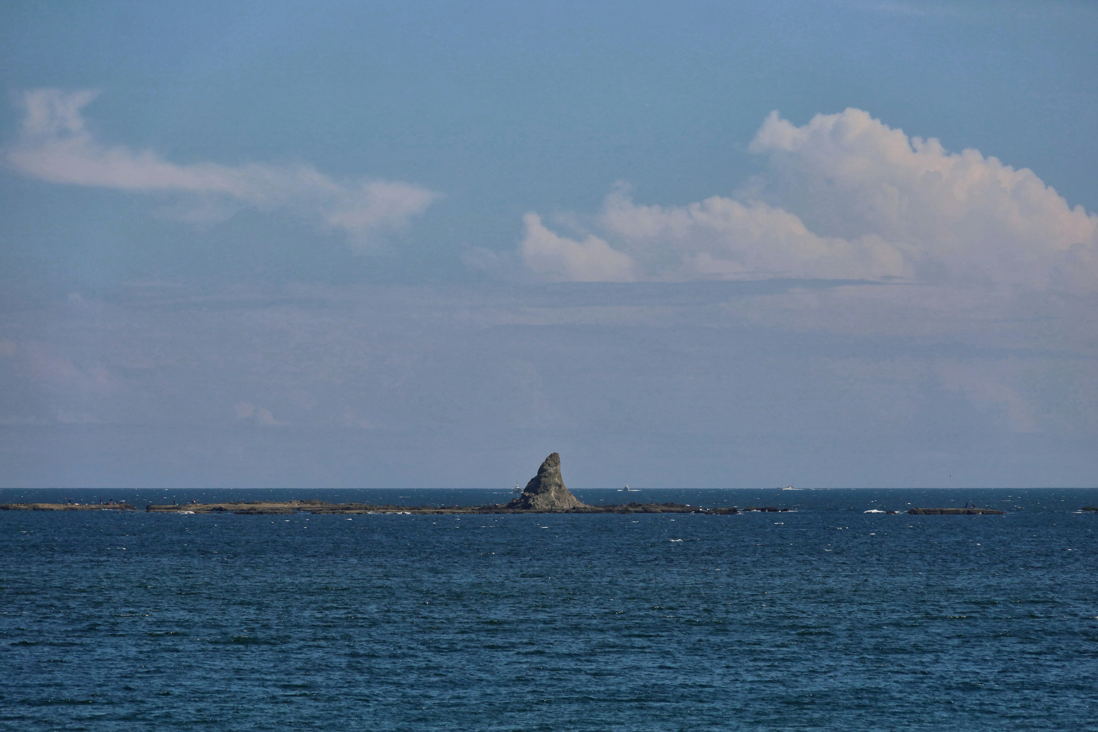 Pequeña roca emergiendo del mar azul bajo un cielo claro con nubes blancas