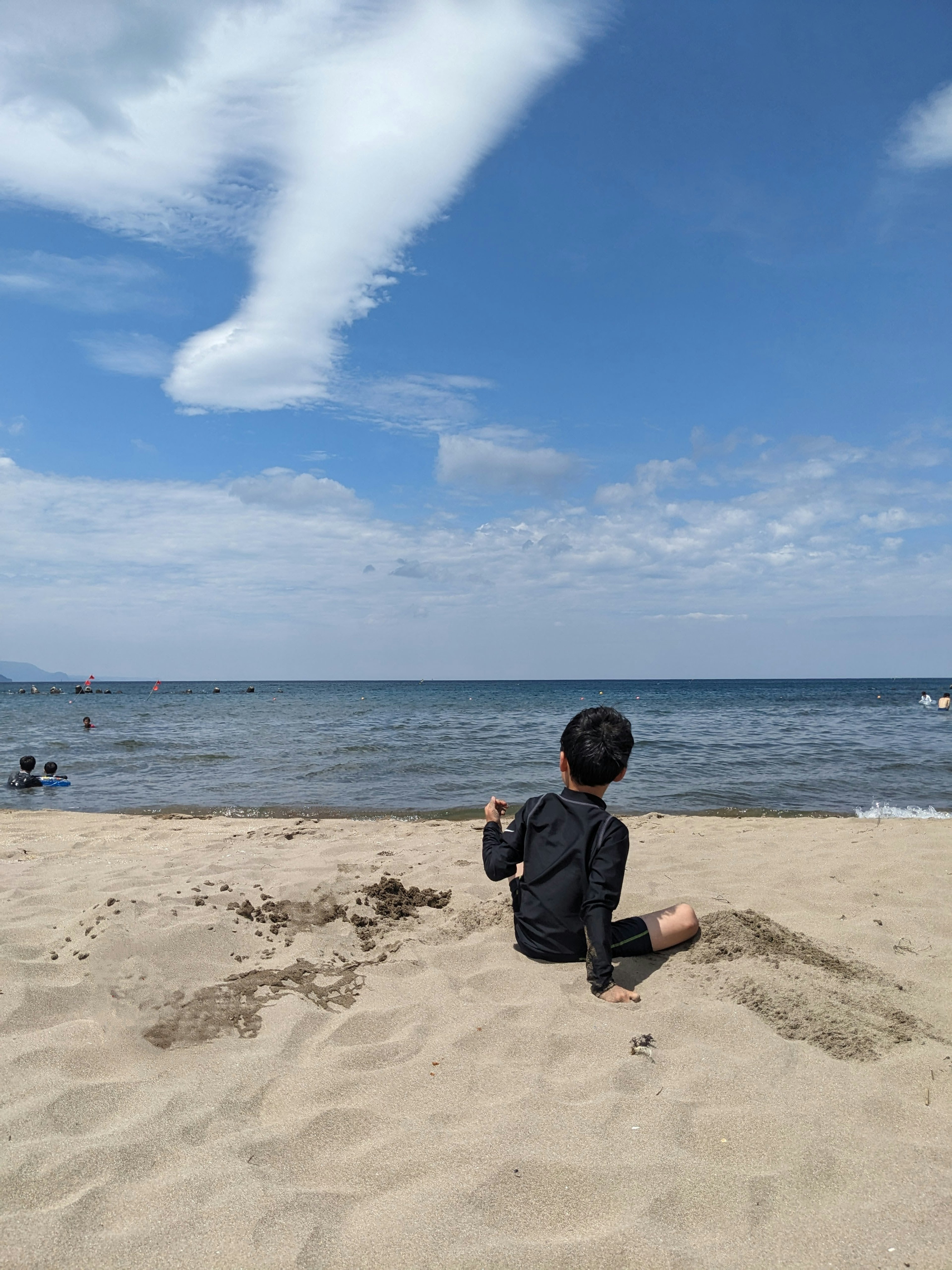 Anak duduk di pantai berpasir dengan lautan dan langit biru