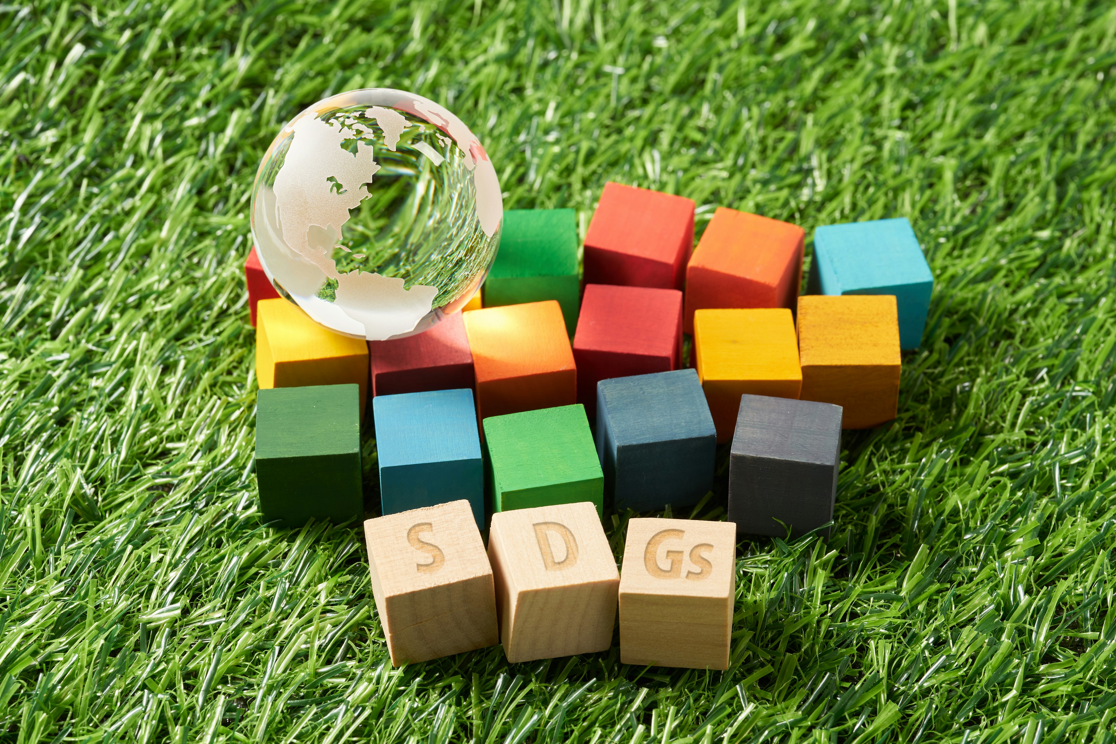 Colorful wooden blocks with SDGs letters and a crystal globe on green grass