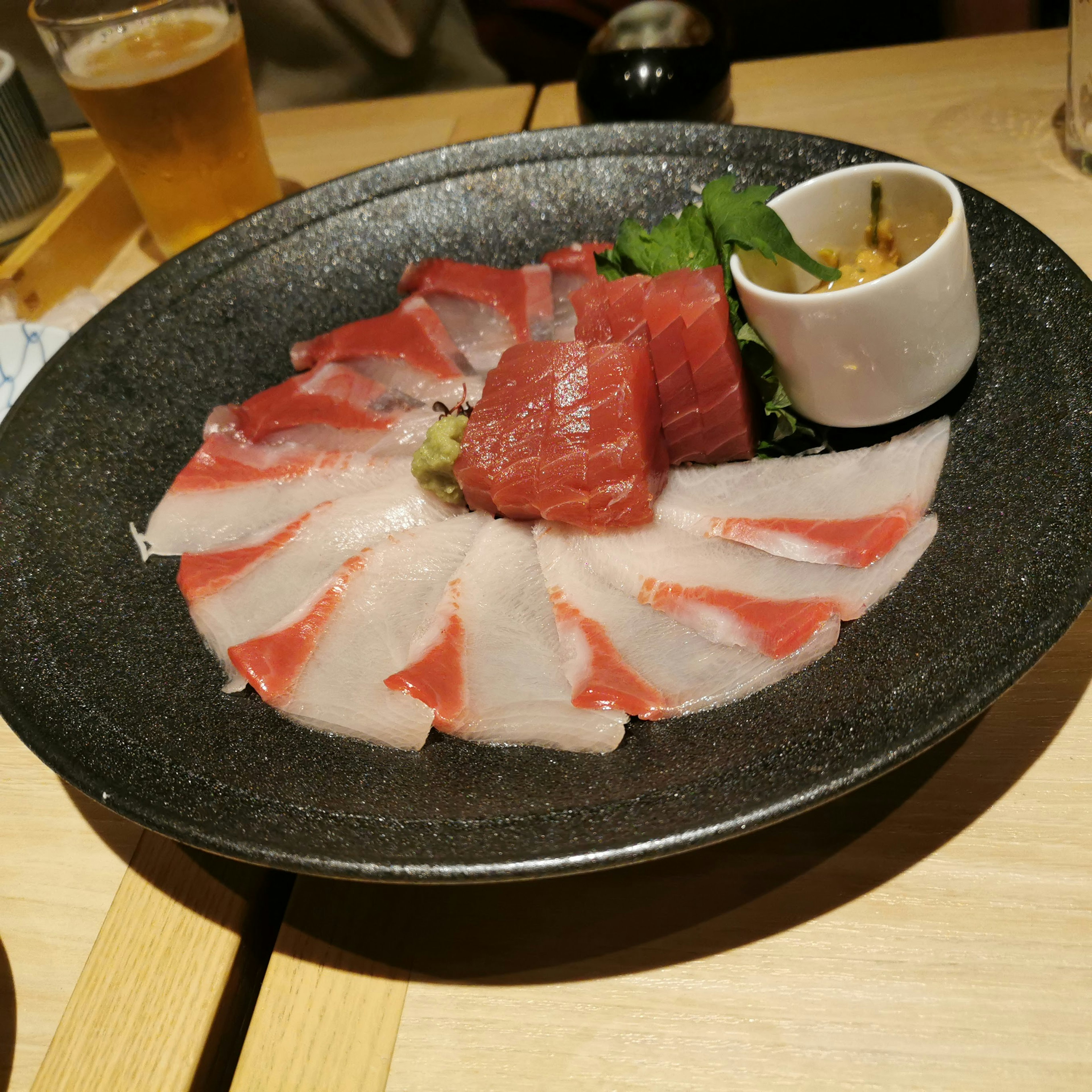 Fresh sashimi arranged on a black plate featuring red and white fish in a circular pattern