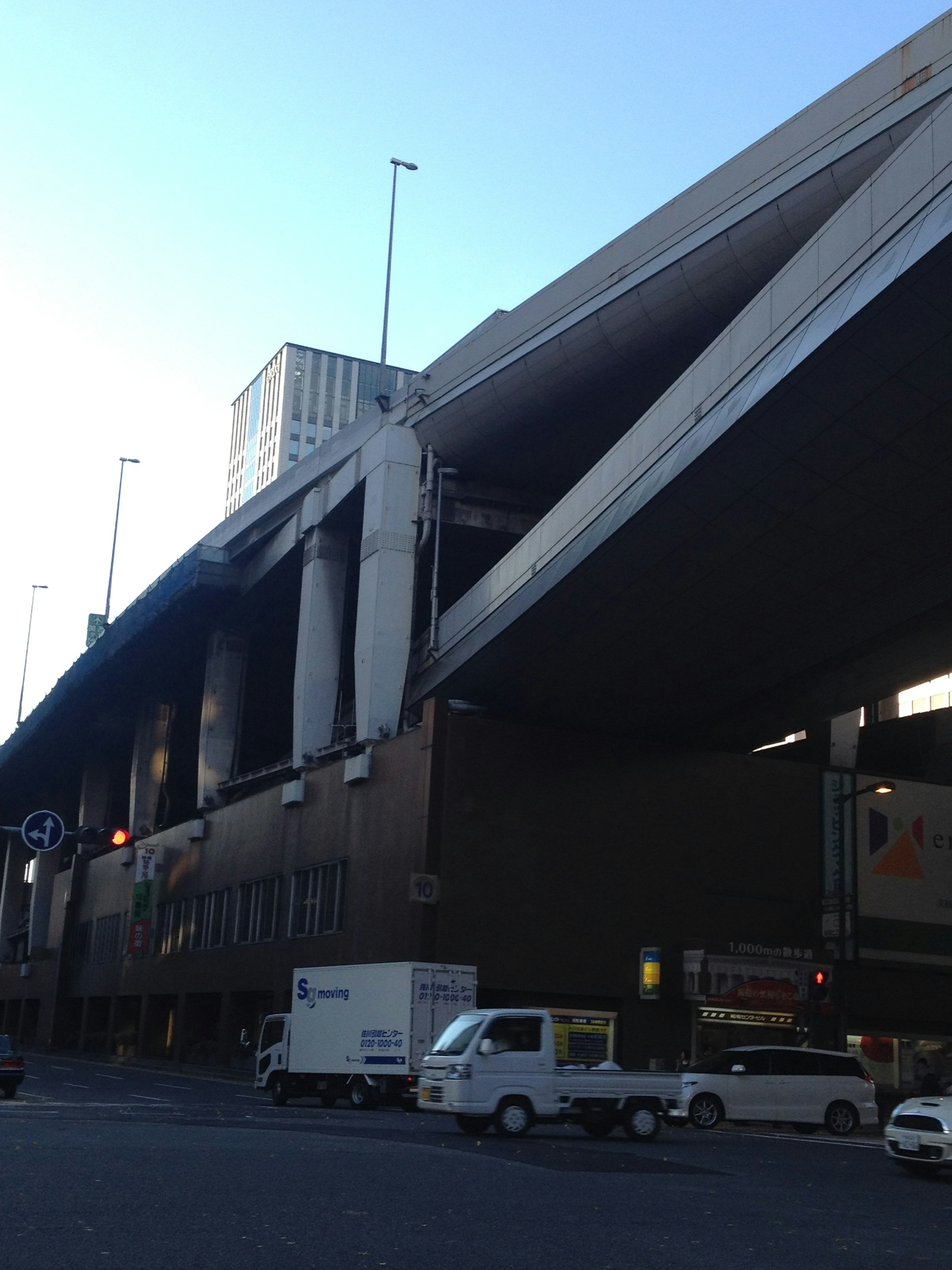 Urban scene featuring a building beneath an overpass with delivery trucks