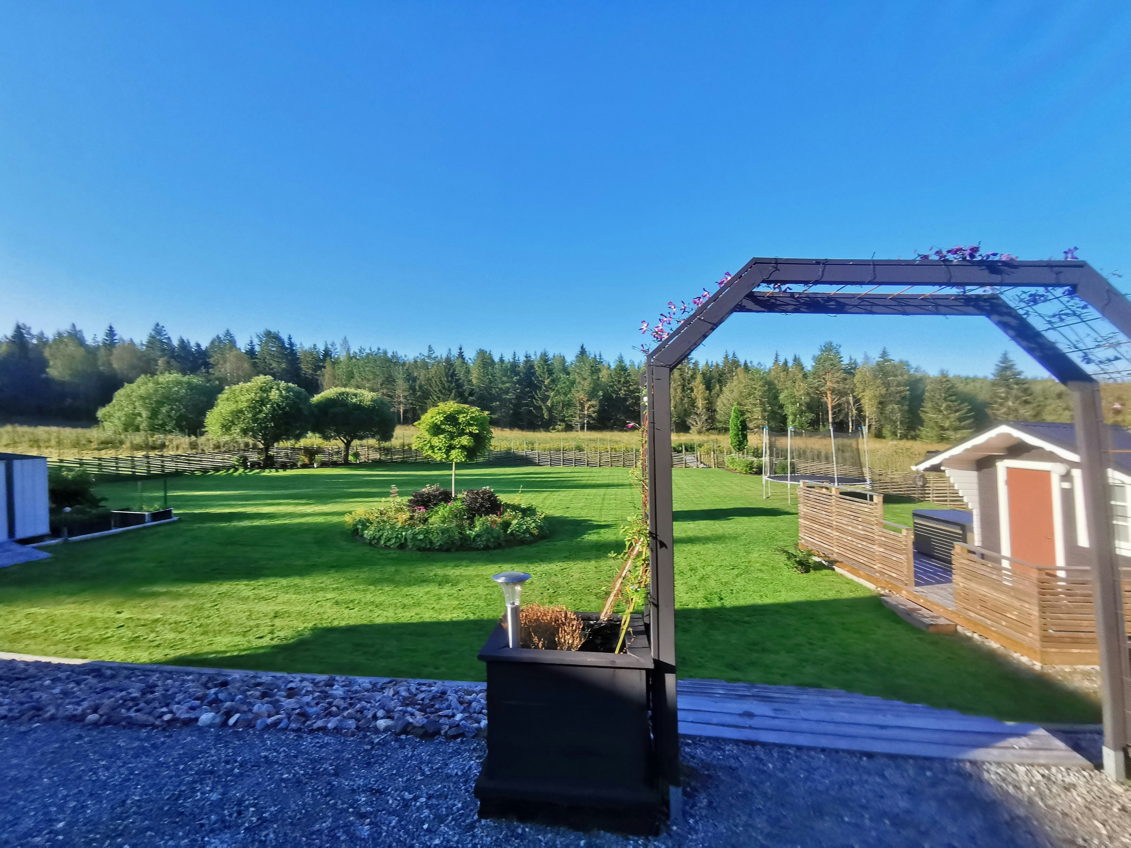 Lush green landscape with trees and a clear blue sky featuring a small shed