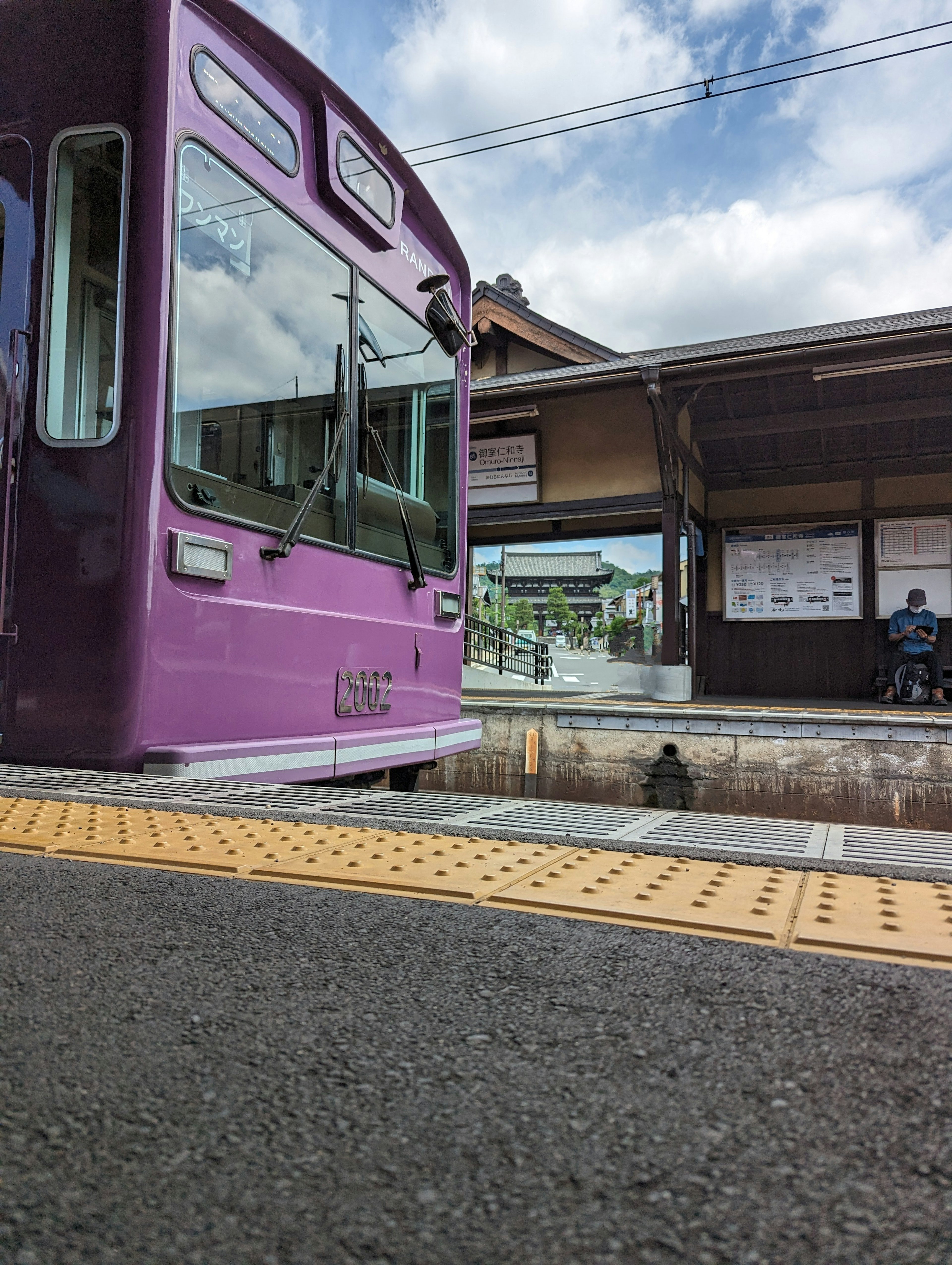 Un train violet à une gare avec un quai et un ciel bleu