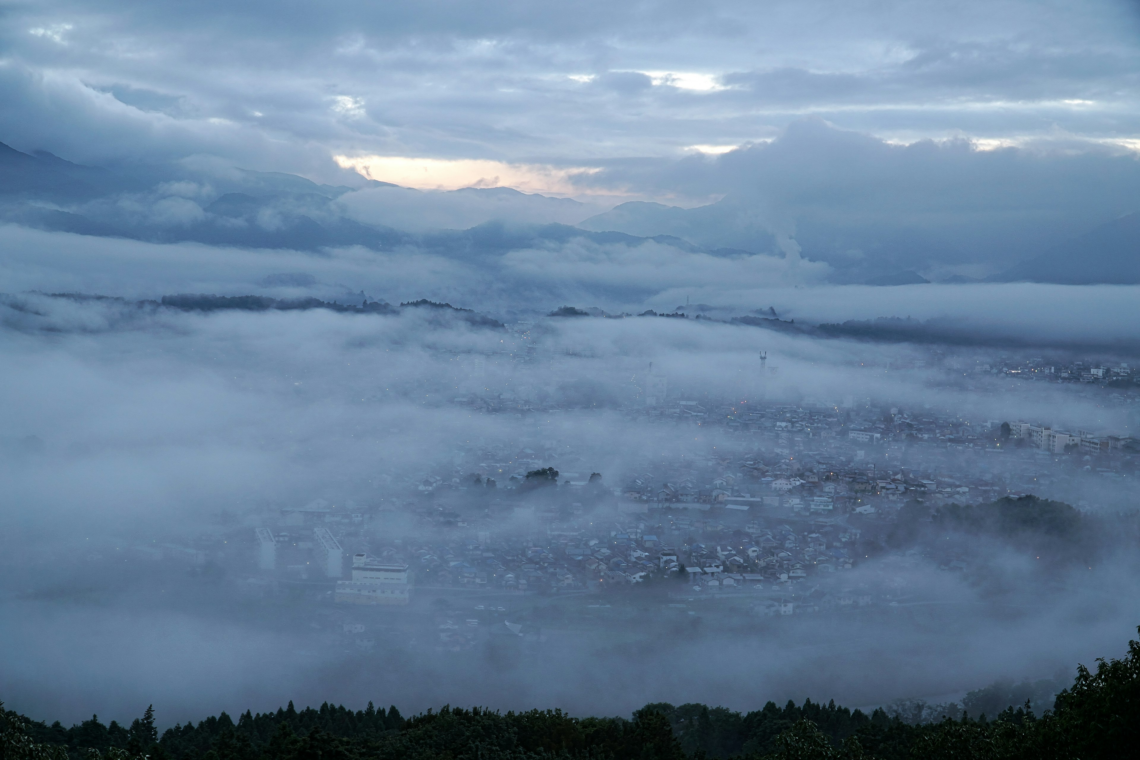 Vista aérea de una ciudad envuelta en niebla con cielo azul y nubes al anochecer