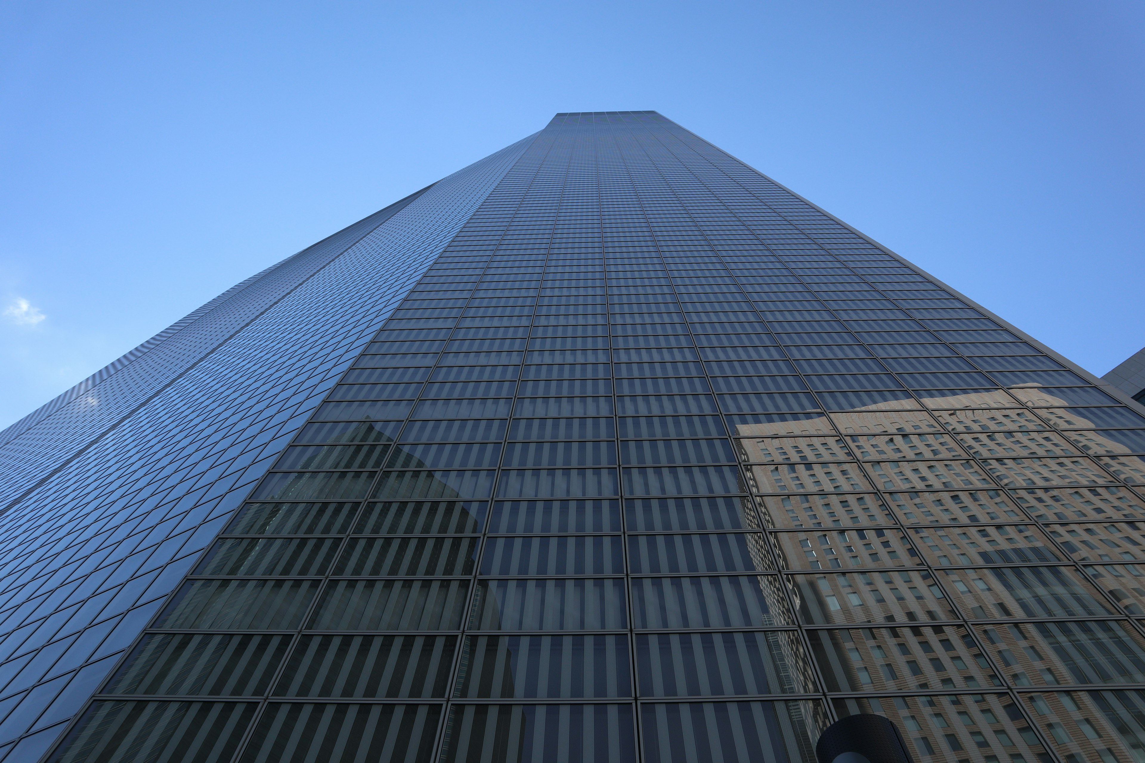 View looking up at a tall glass skyscraper with blue sky