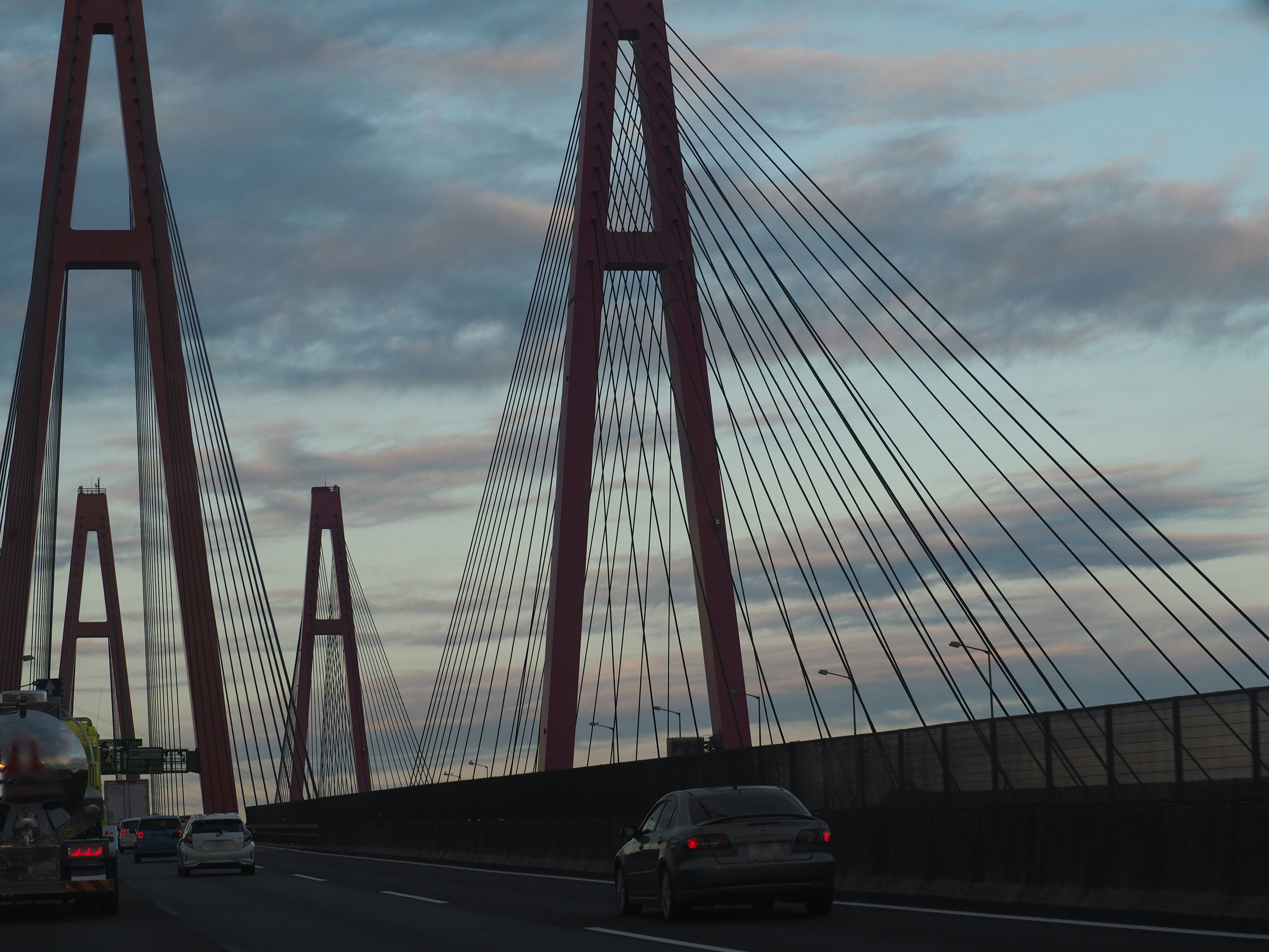 Pont à haubans rouge avec une route et un ciel nuageux