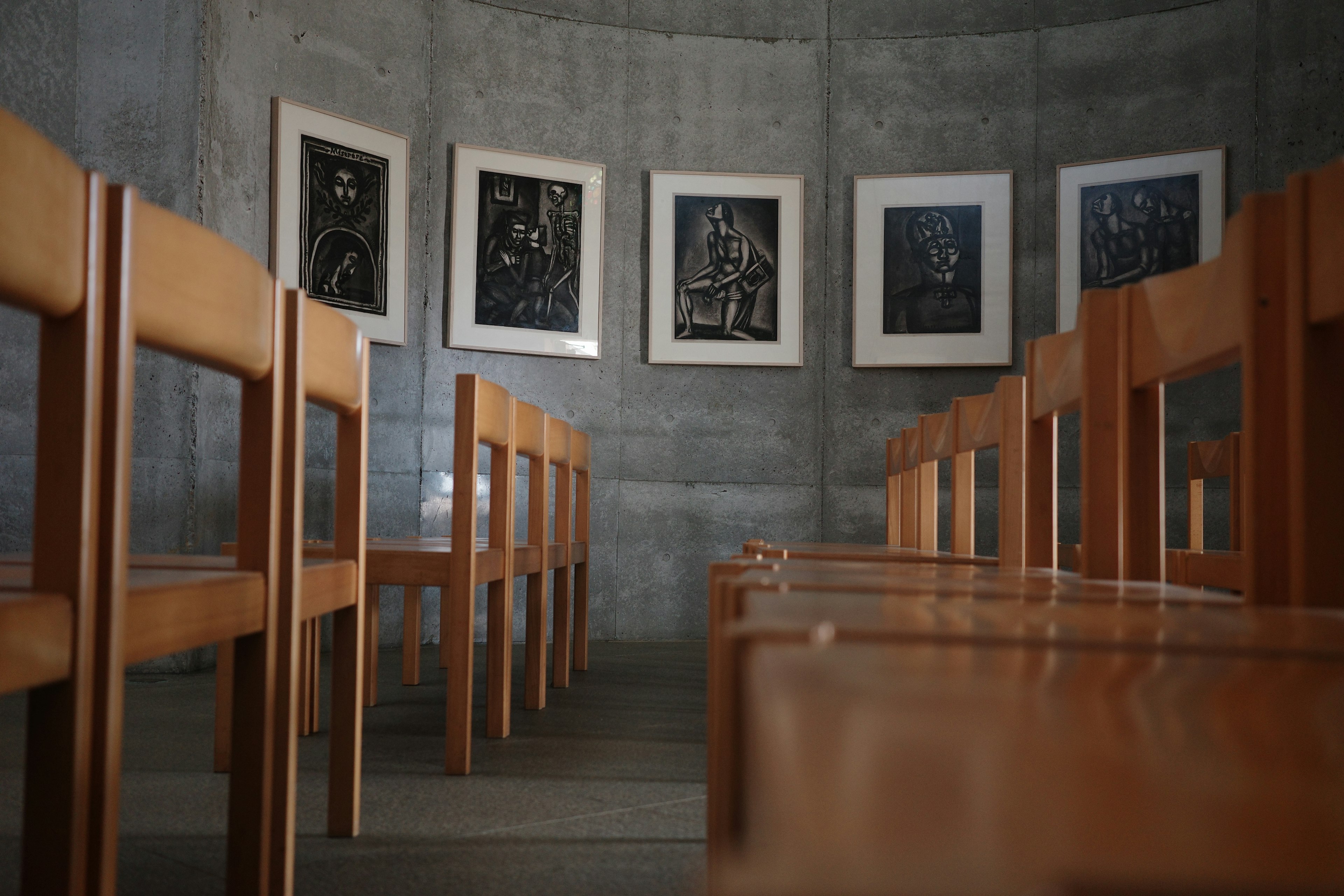 Wooden chairs arranged in a concrete room with framed artworks on the walls