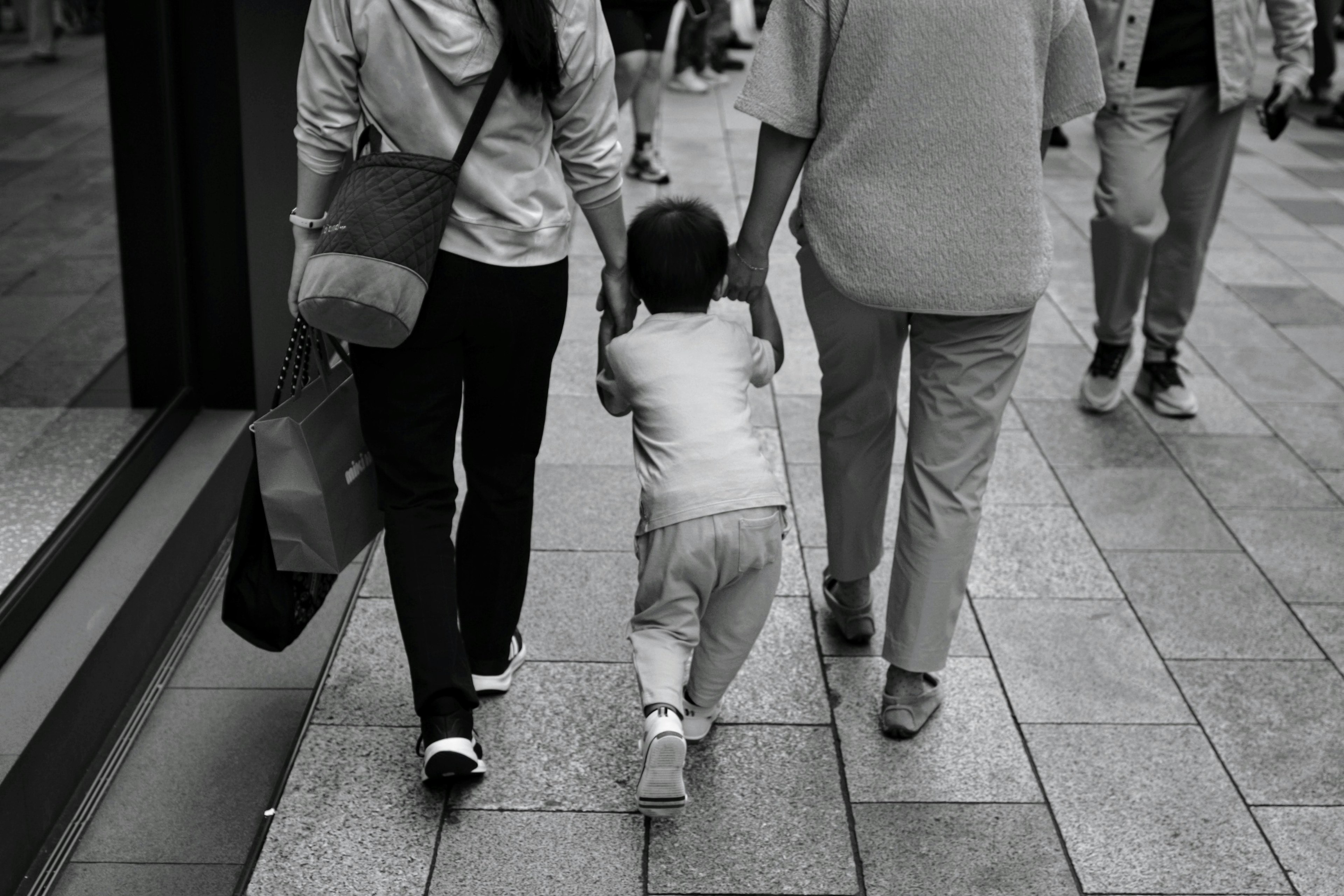 親と子供が手をつないで歩くモノクロの街並み