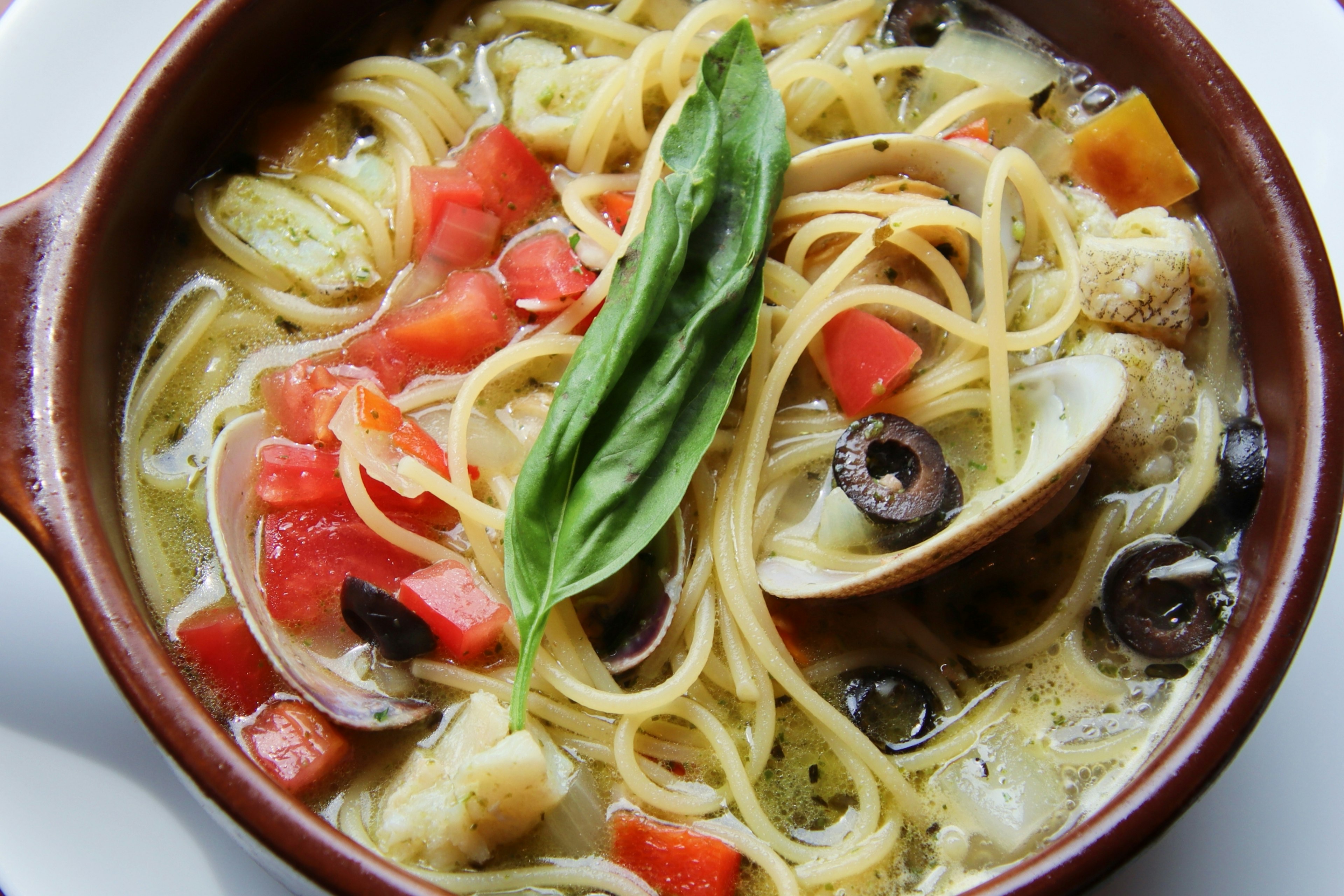 A bowl of spaghetti with vegetables and basil leaf on top