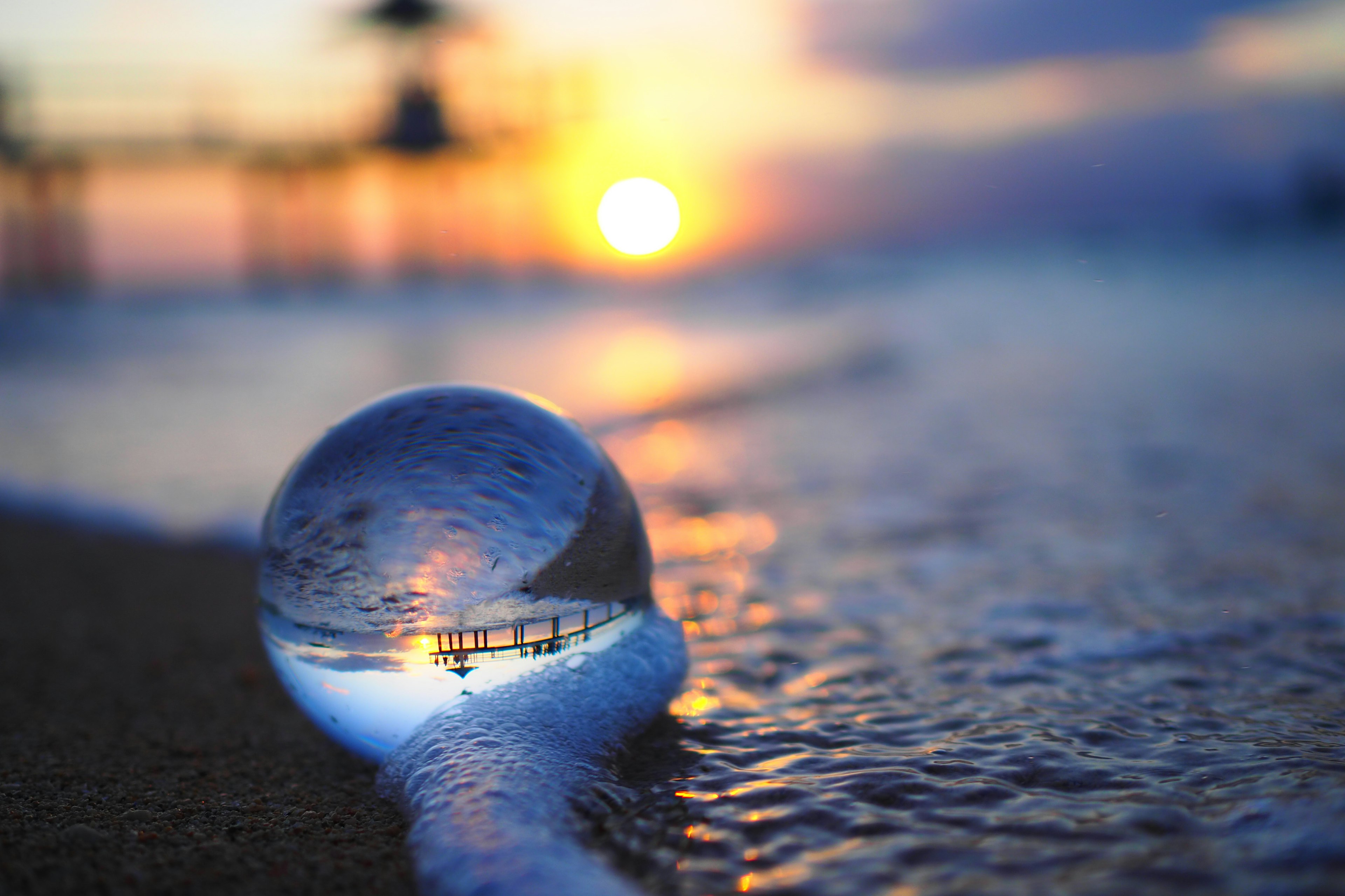 A glass sphere on the shoreline reflecting the sunset