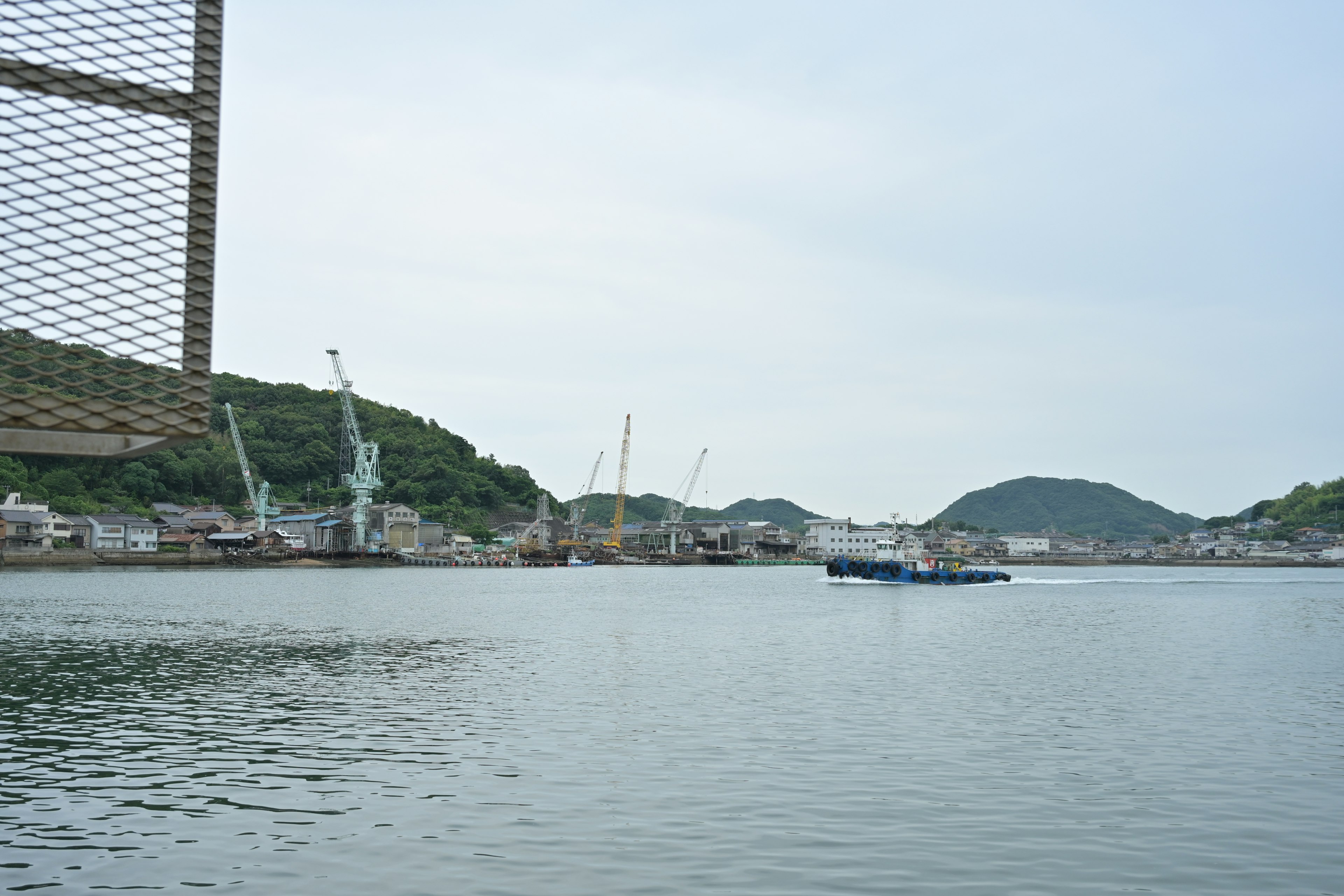 View of a boat on the water with cranes and hills in the background