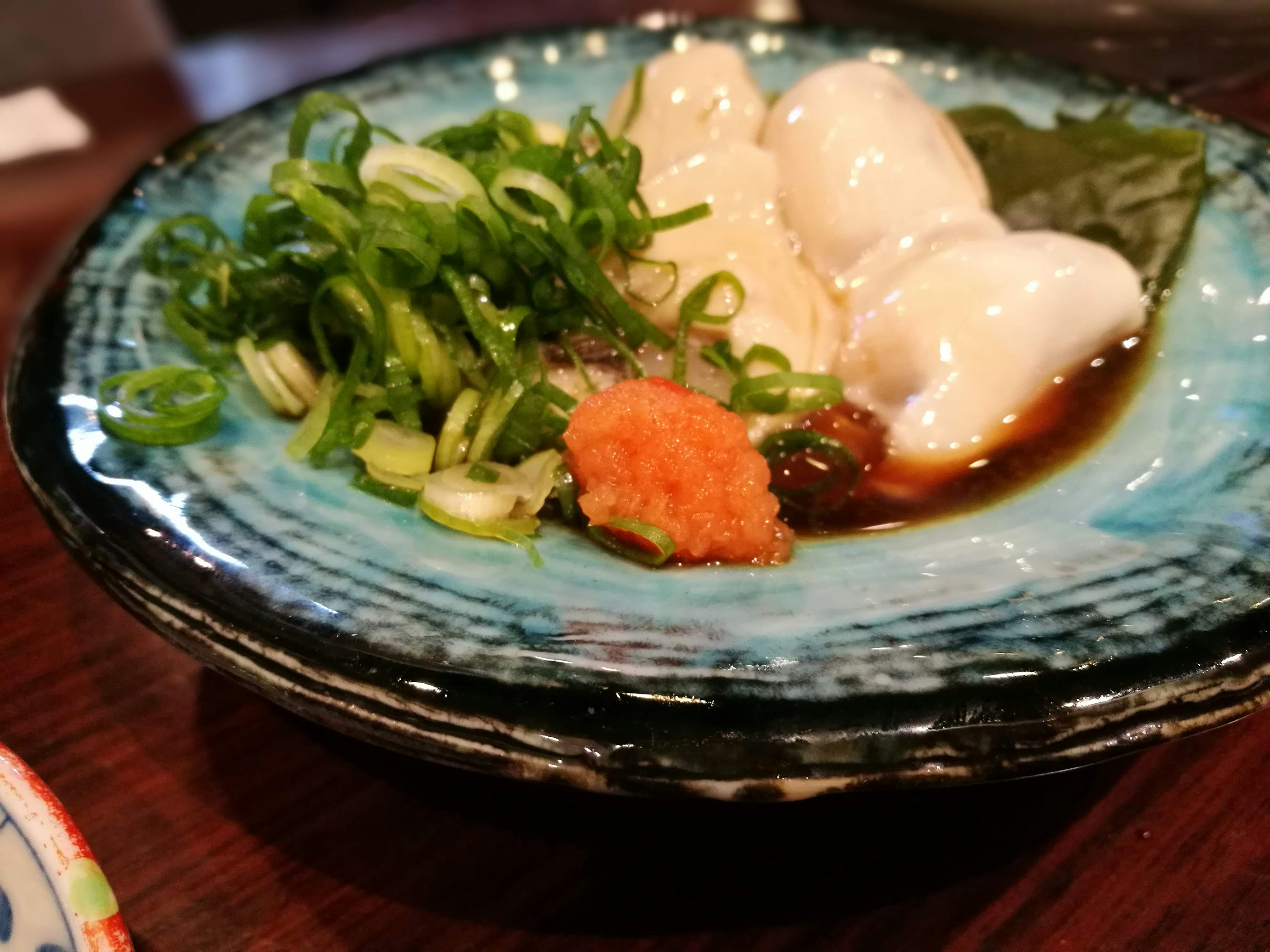 Dumplings served on a blue plate with green onions and wasabi