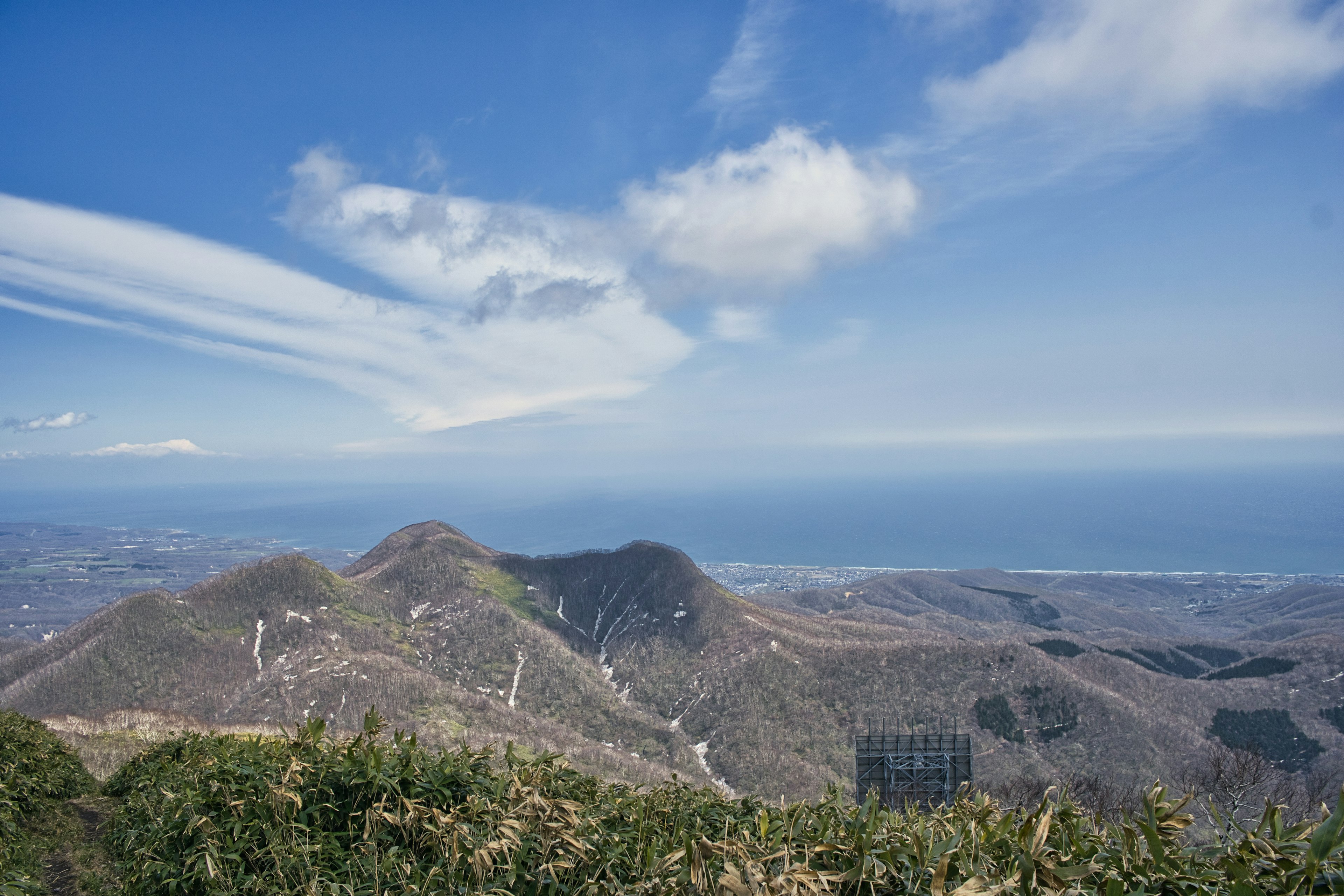 Pemandangan panorama pegunungan dikelilingi langit biru dan awan dengan lautan jauh