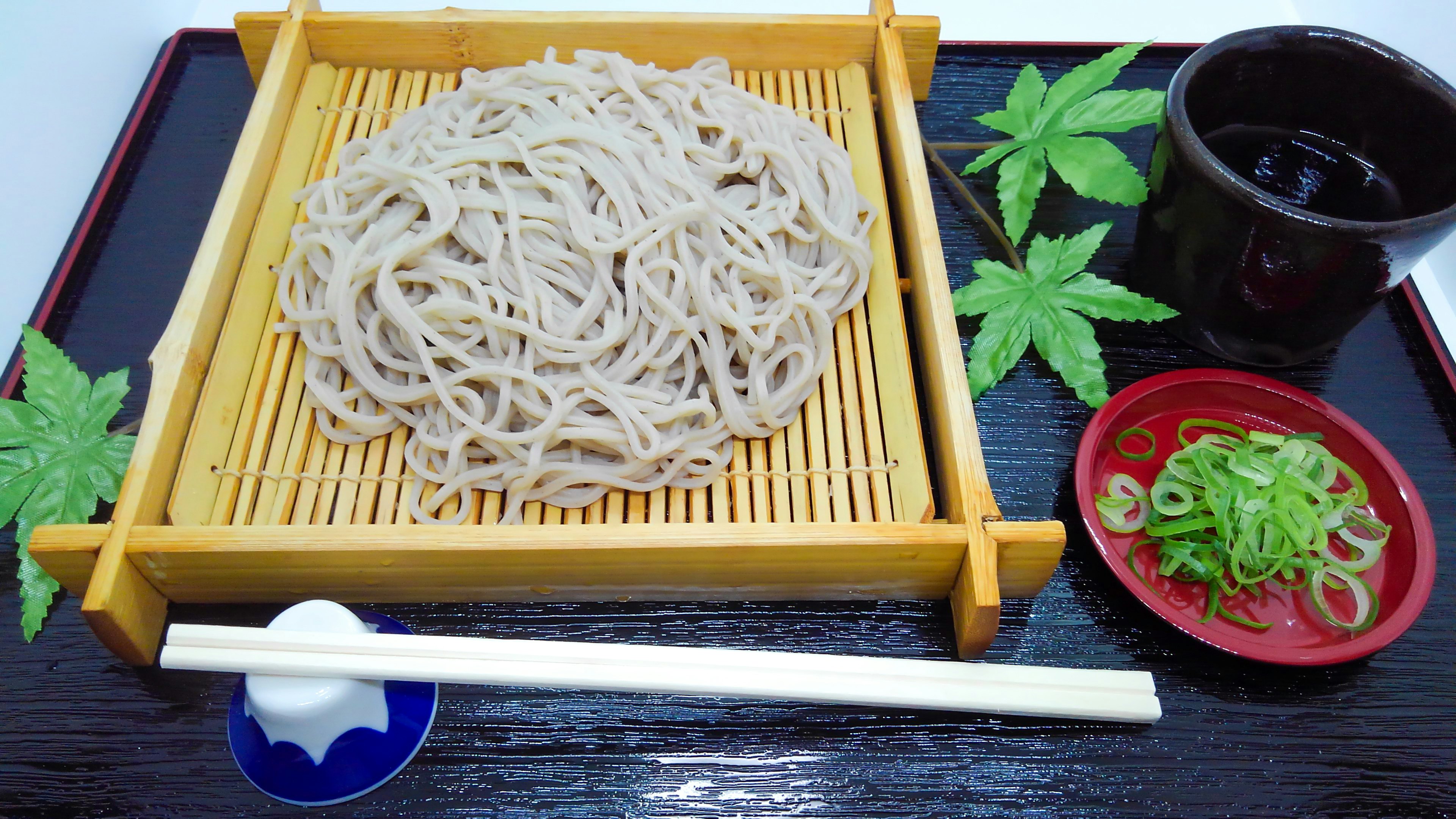 Soba auf einem Bambusgestell mit Frühlingszwiebeln und Dipsauce serviert