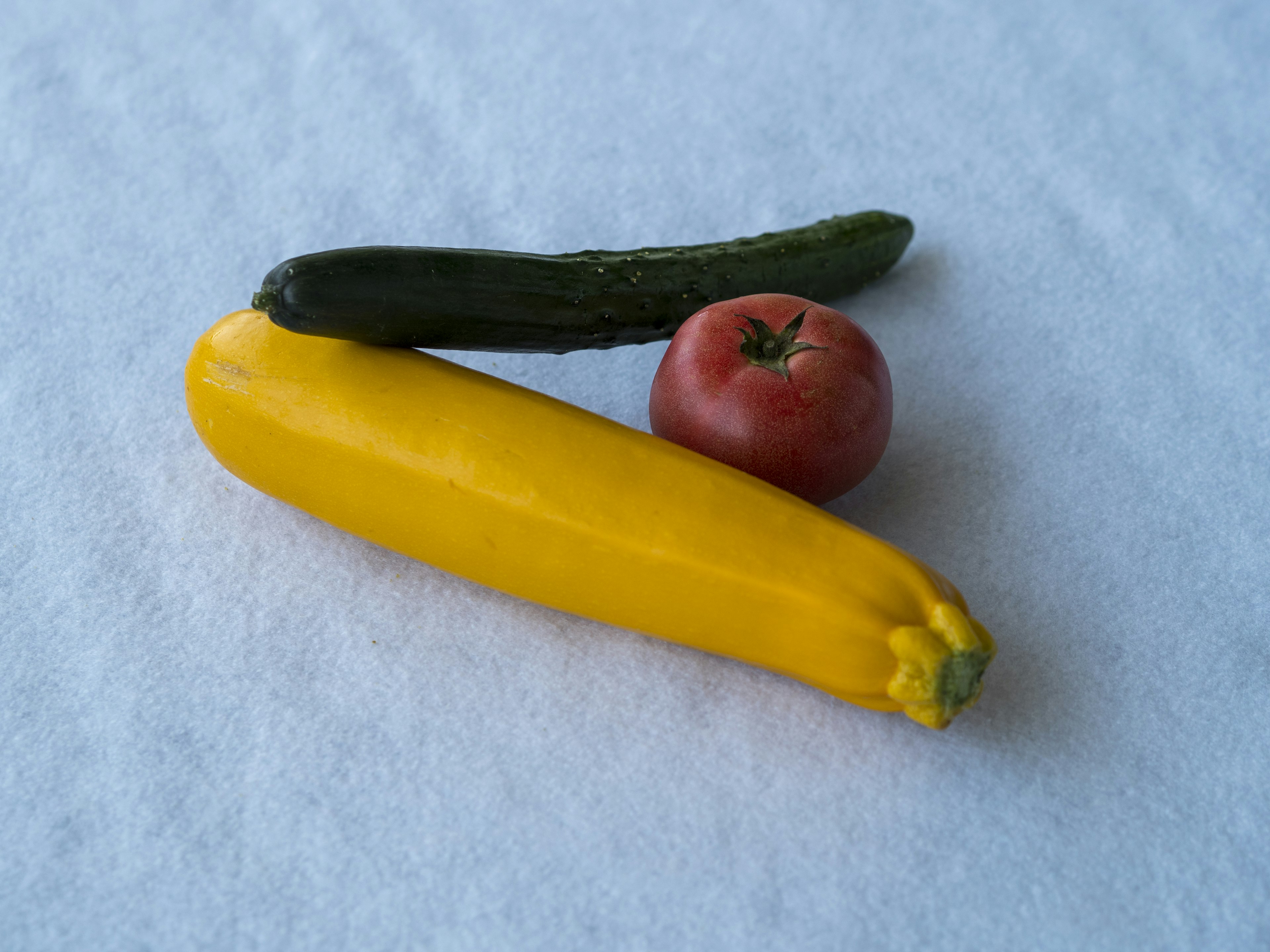 Sebuah zucchini kuning, mentimun hijau, dan tomat merah disusun bersama