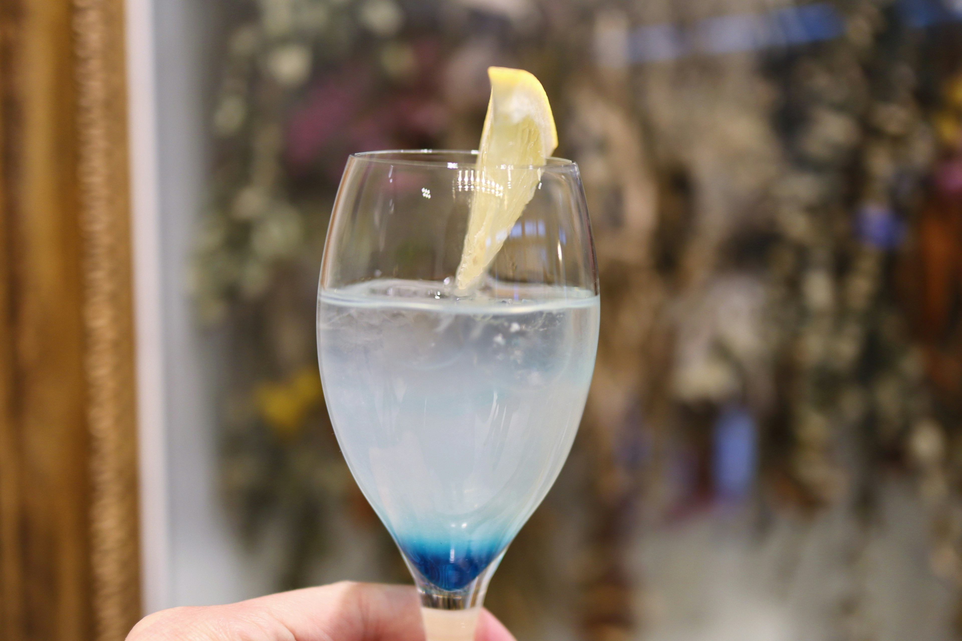 A clear glass with a blue drink and a slice of lemon on the rim