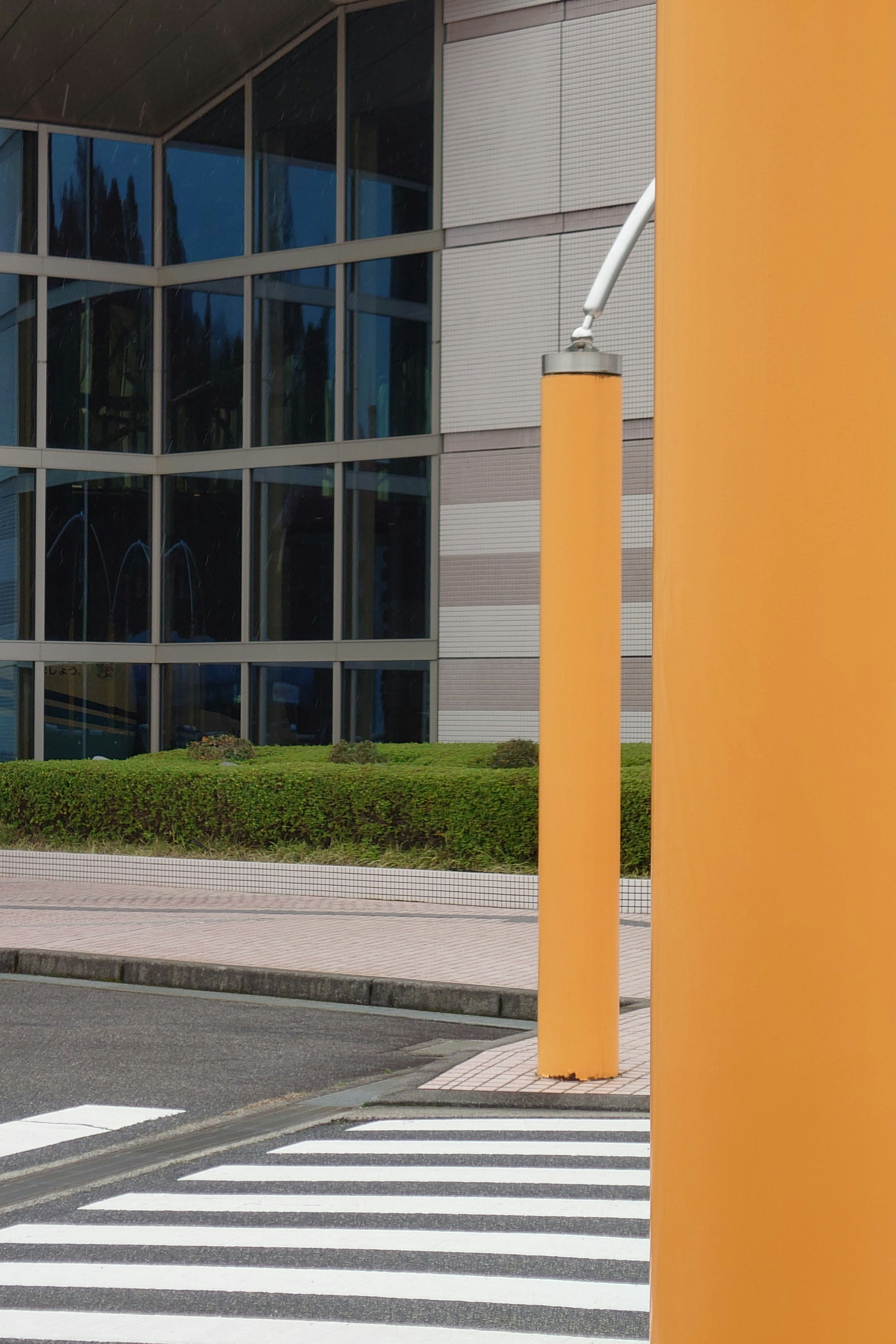 Façade moderne d'un bâtiment avec des poteaux orange et un passage piéton