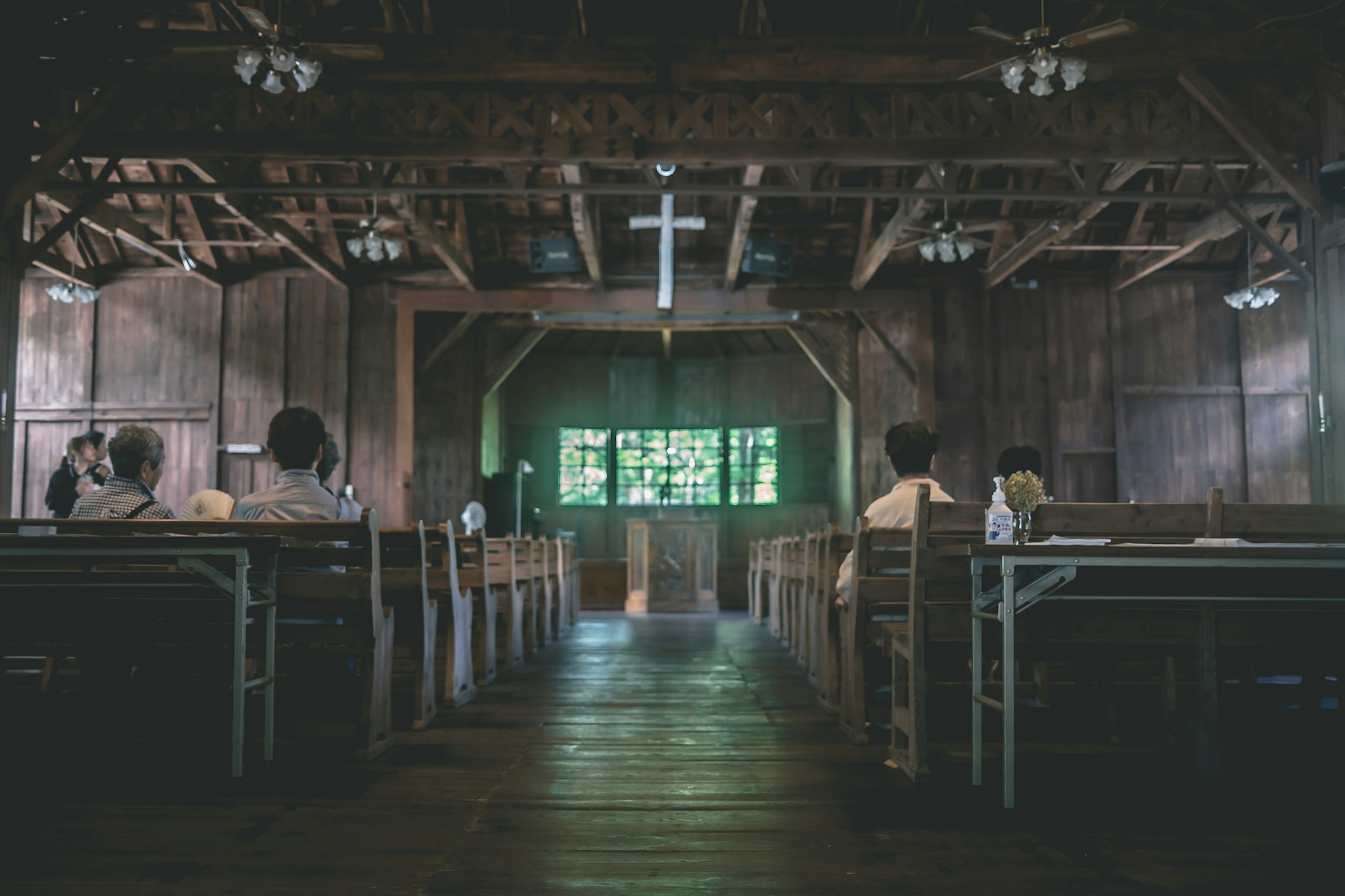 Interior de una iglesia de madera con una cruz y un vitral verde al fondo