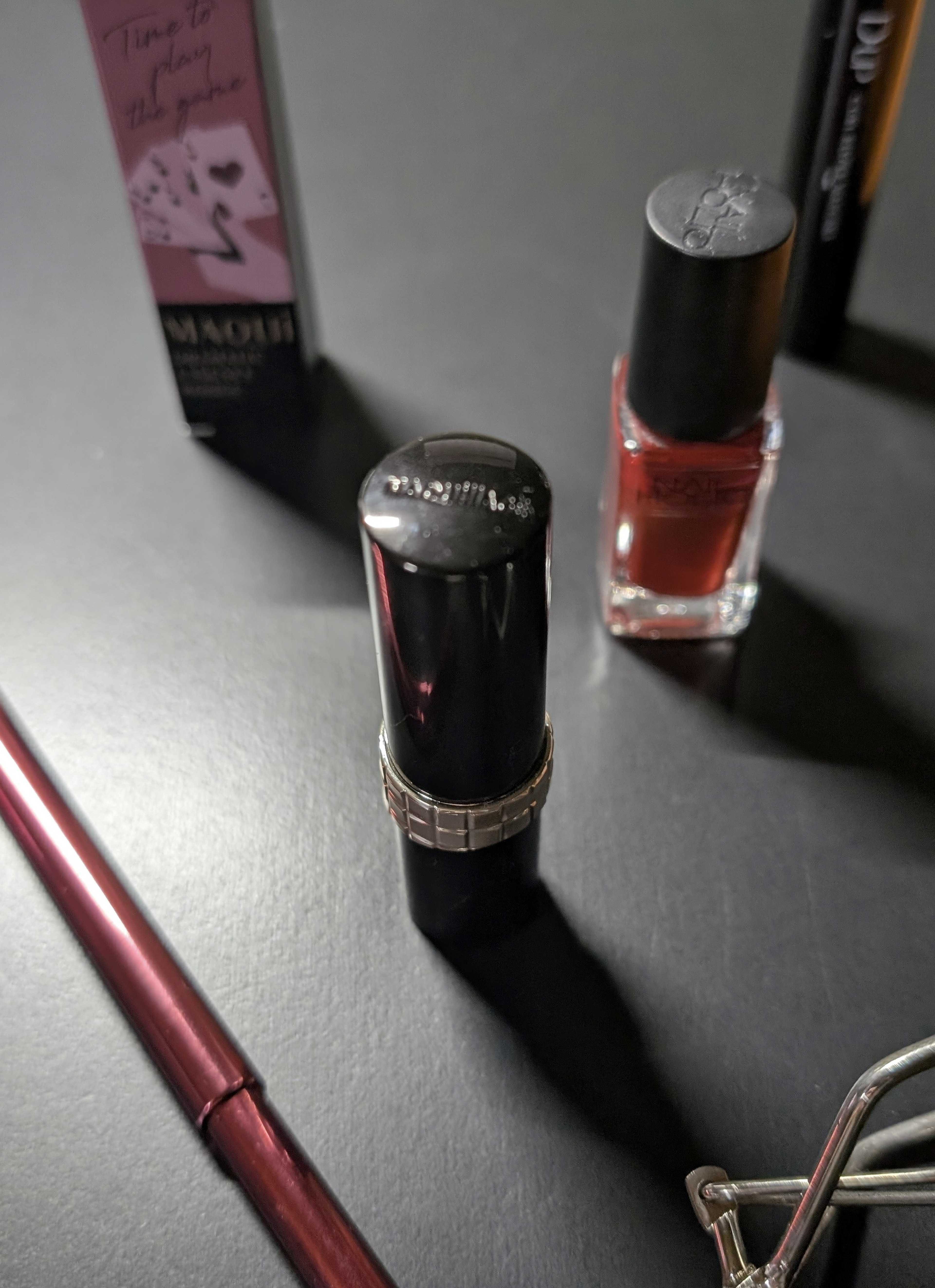 Image of makeup items including a black lipstick and red nail polish