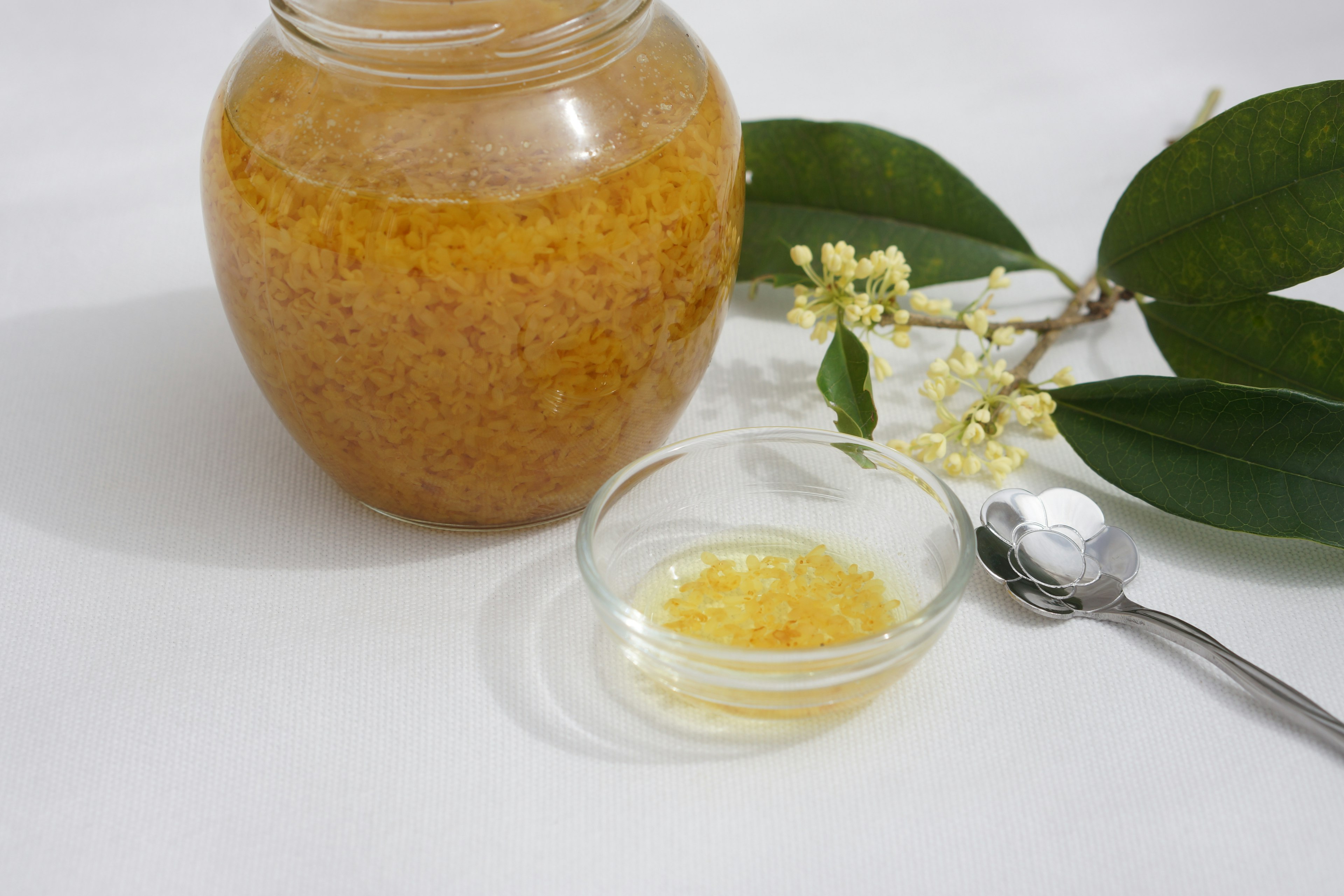 A jar of golden honey with a small dish of honey and green leaves in the background