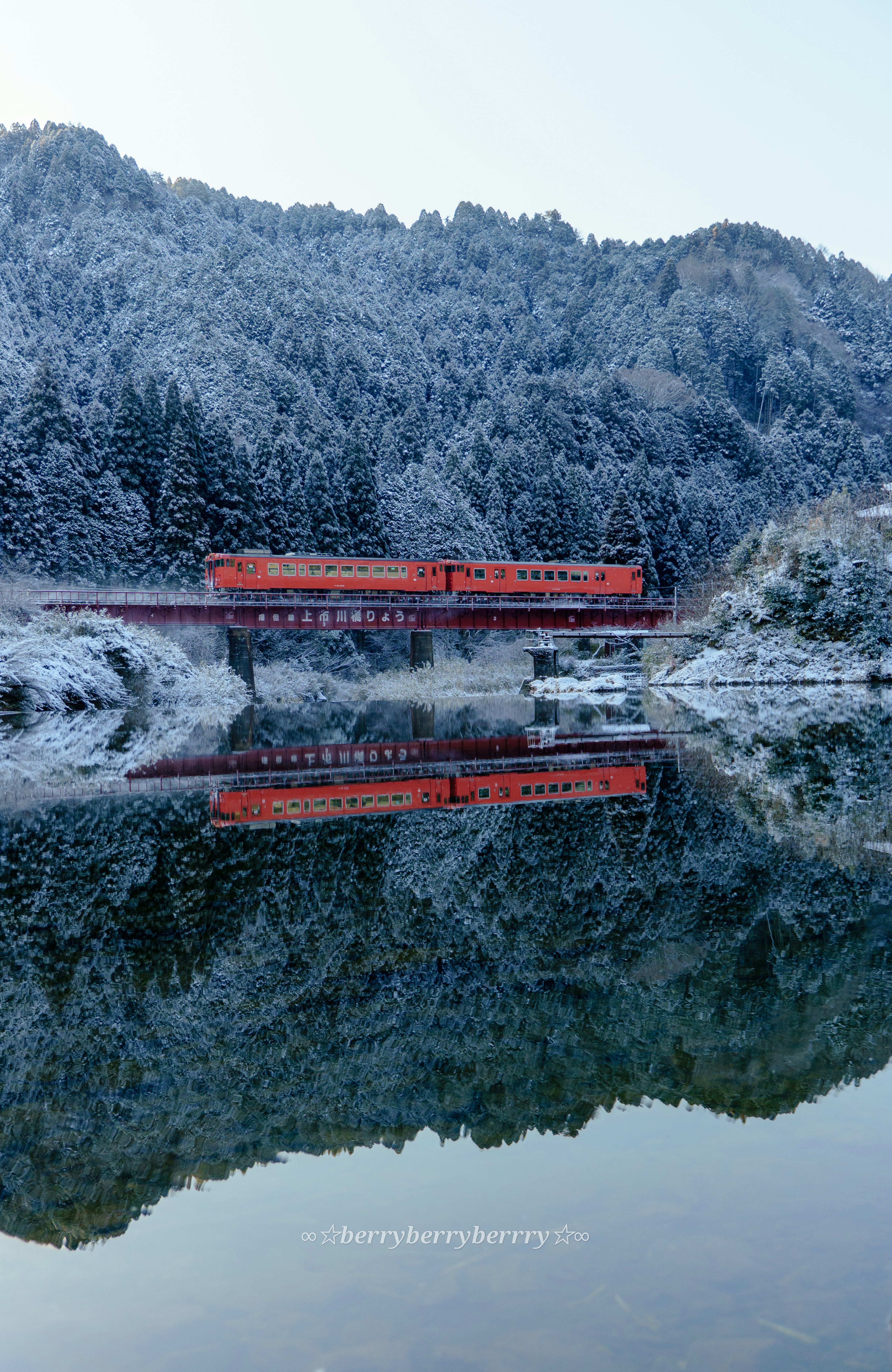 Vista serena di un lago con montagne innevate e il riflesso di un treno rosso