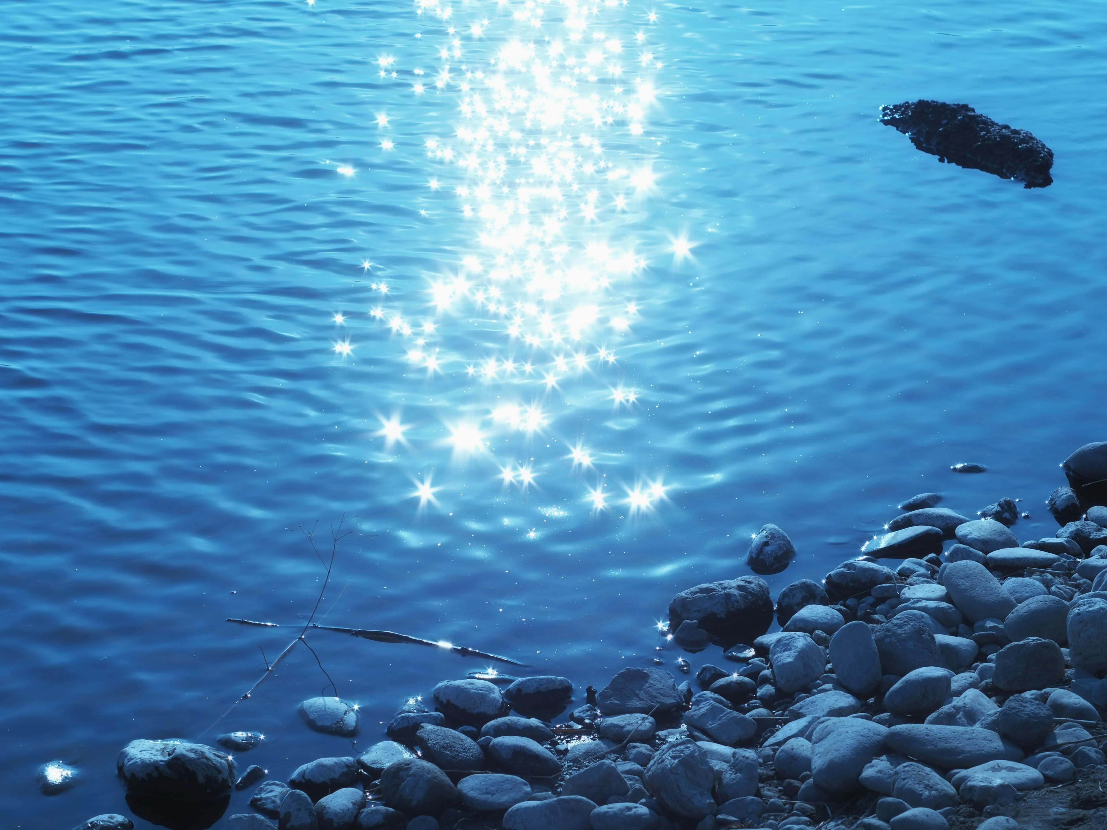 Reflejos brillantes en una superficie de agua azul con una orilla rocosa