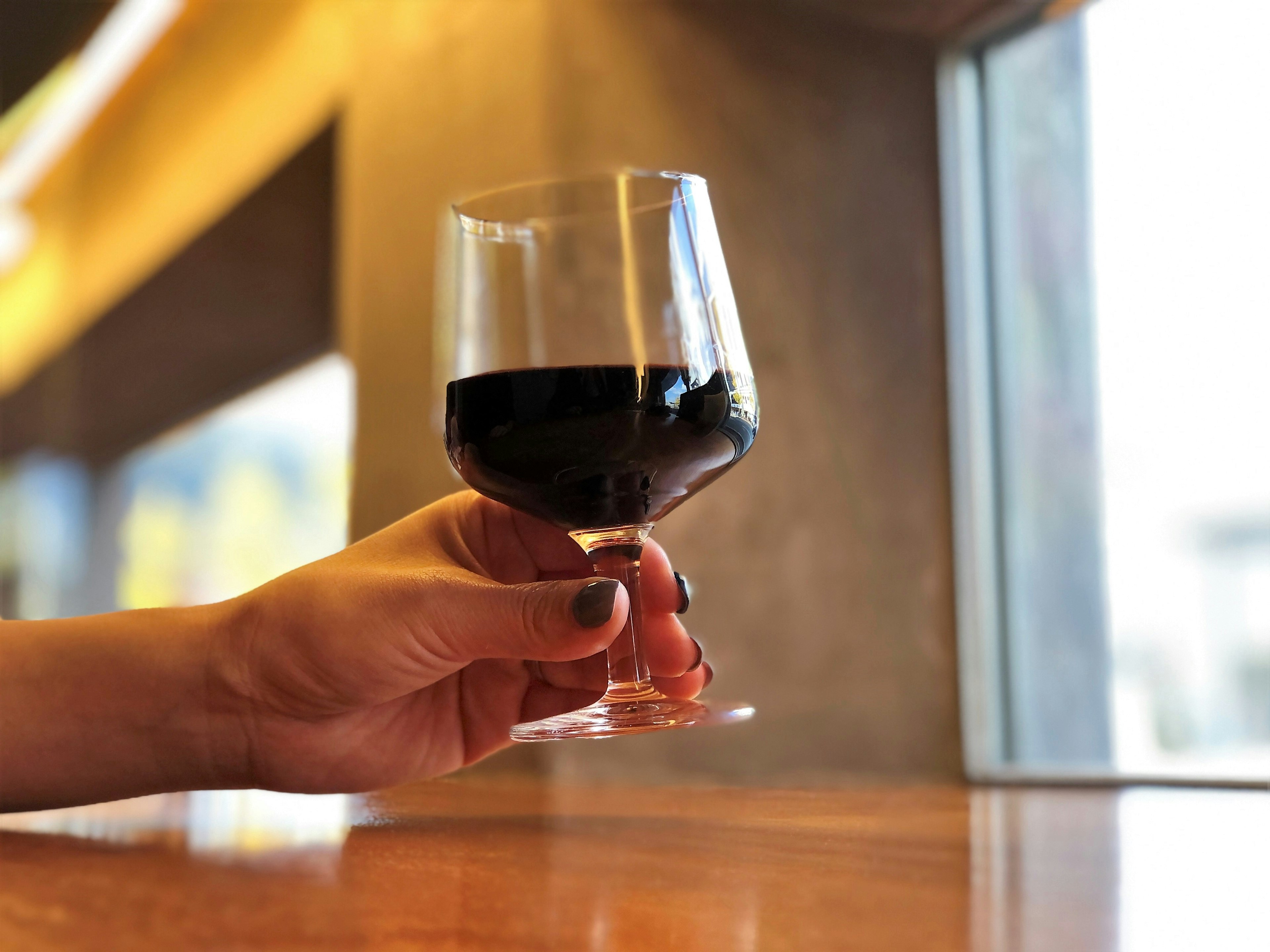 A hand holding a glass of red wine in a casual interior setting