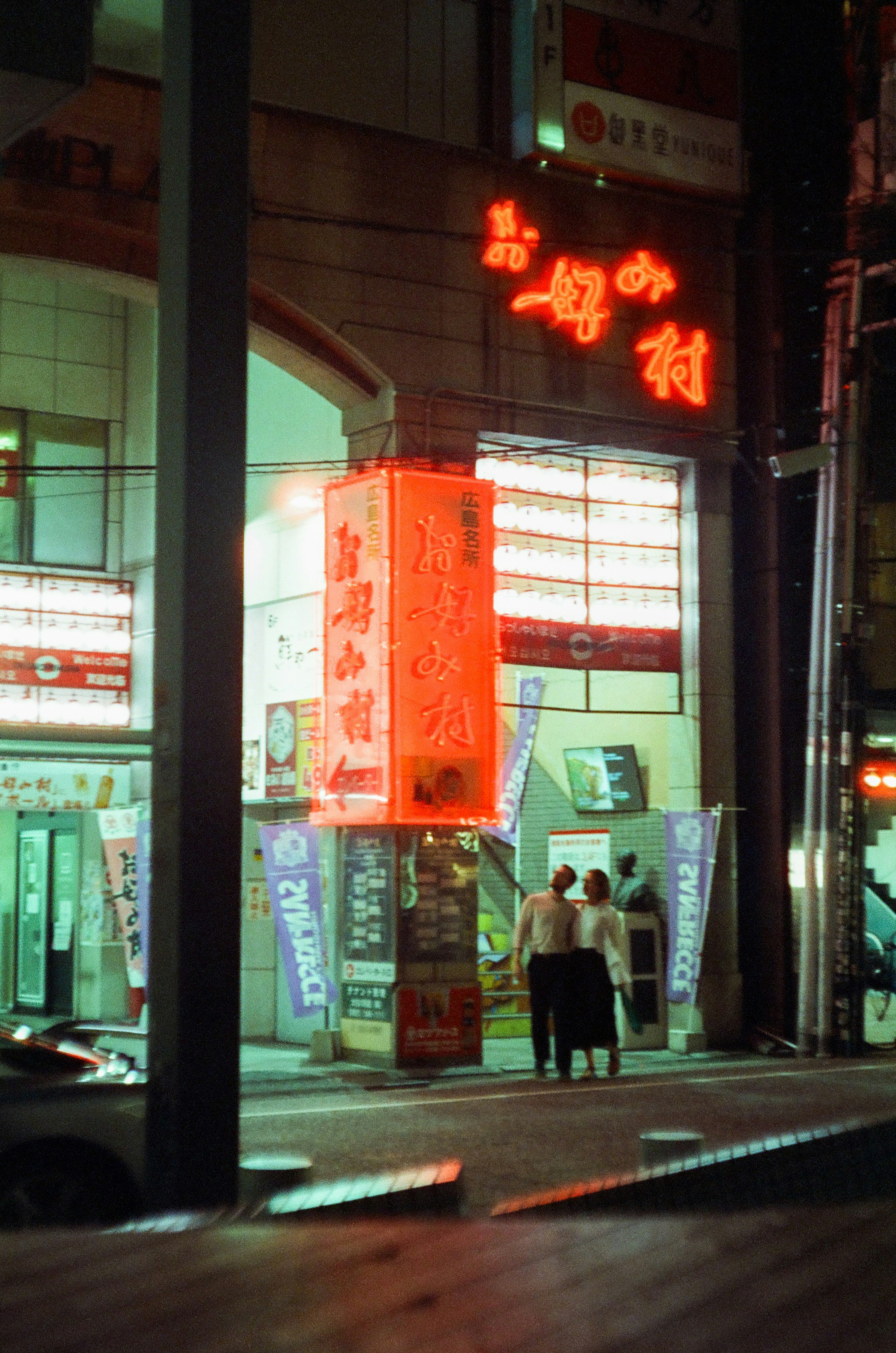 Couple standing outside a restaurant with bright red signage at night