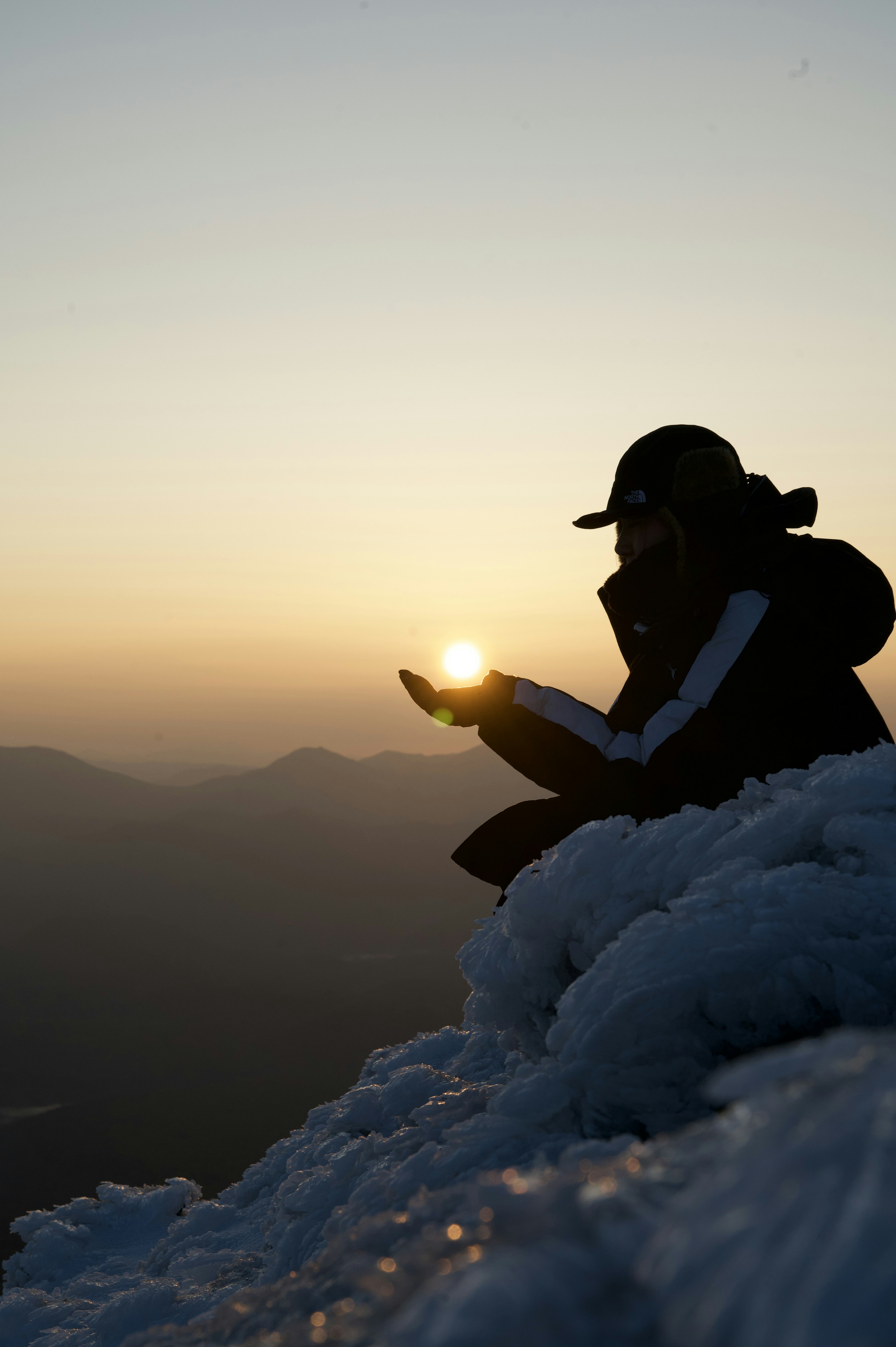 夕日を手のひらに乗せるシルエットの登山者