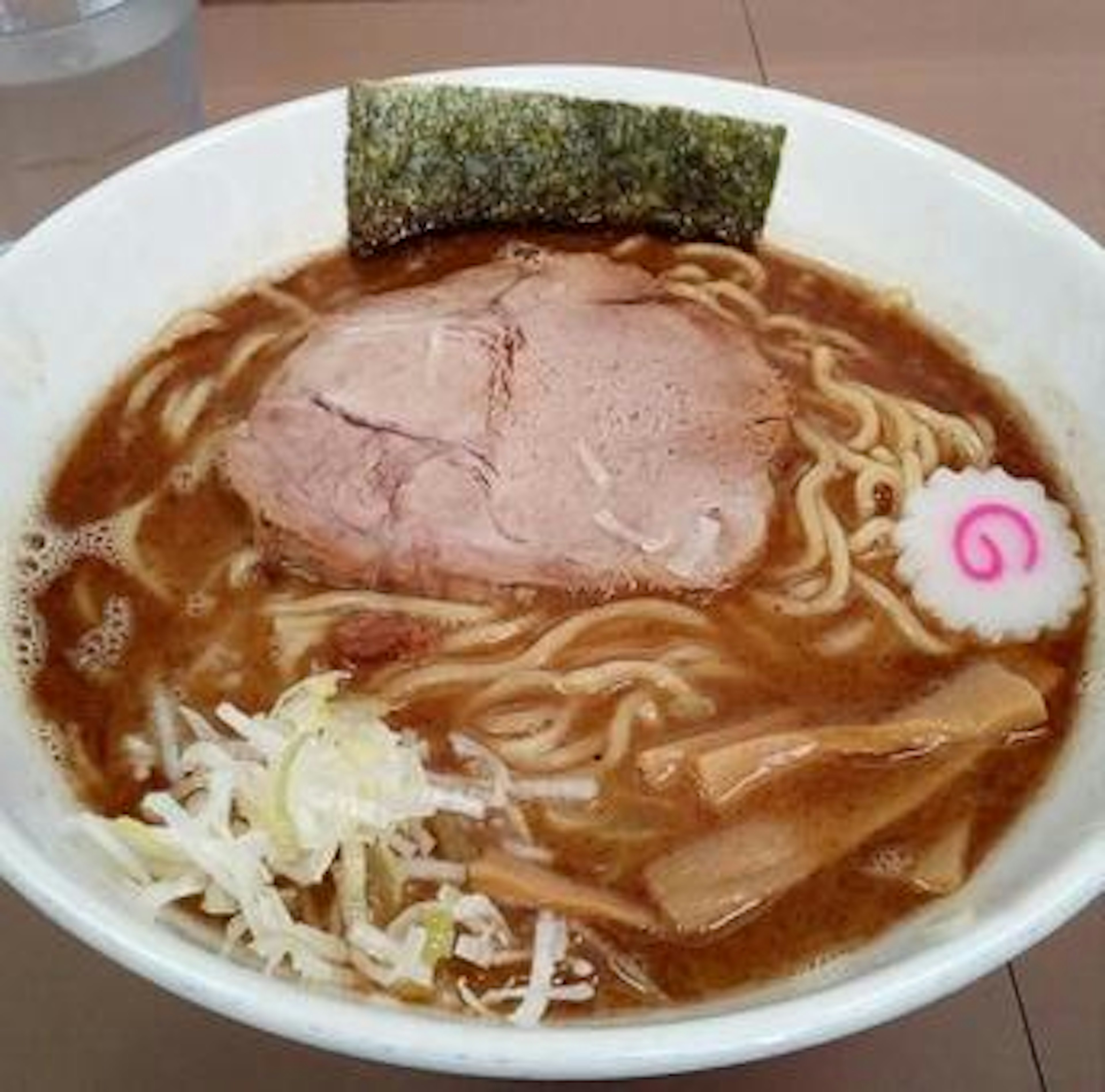 ラーメンのボウルにチャーシュー、ナルト、メンマ、キャベツが入っている