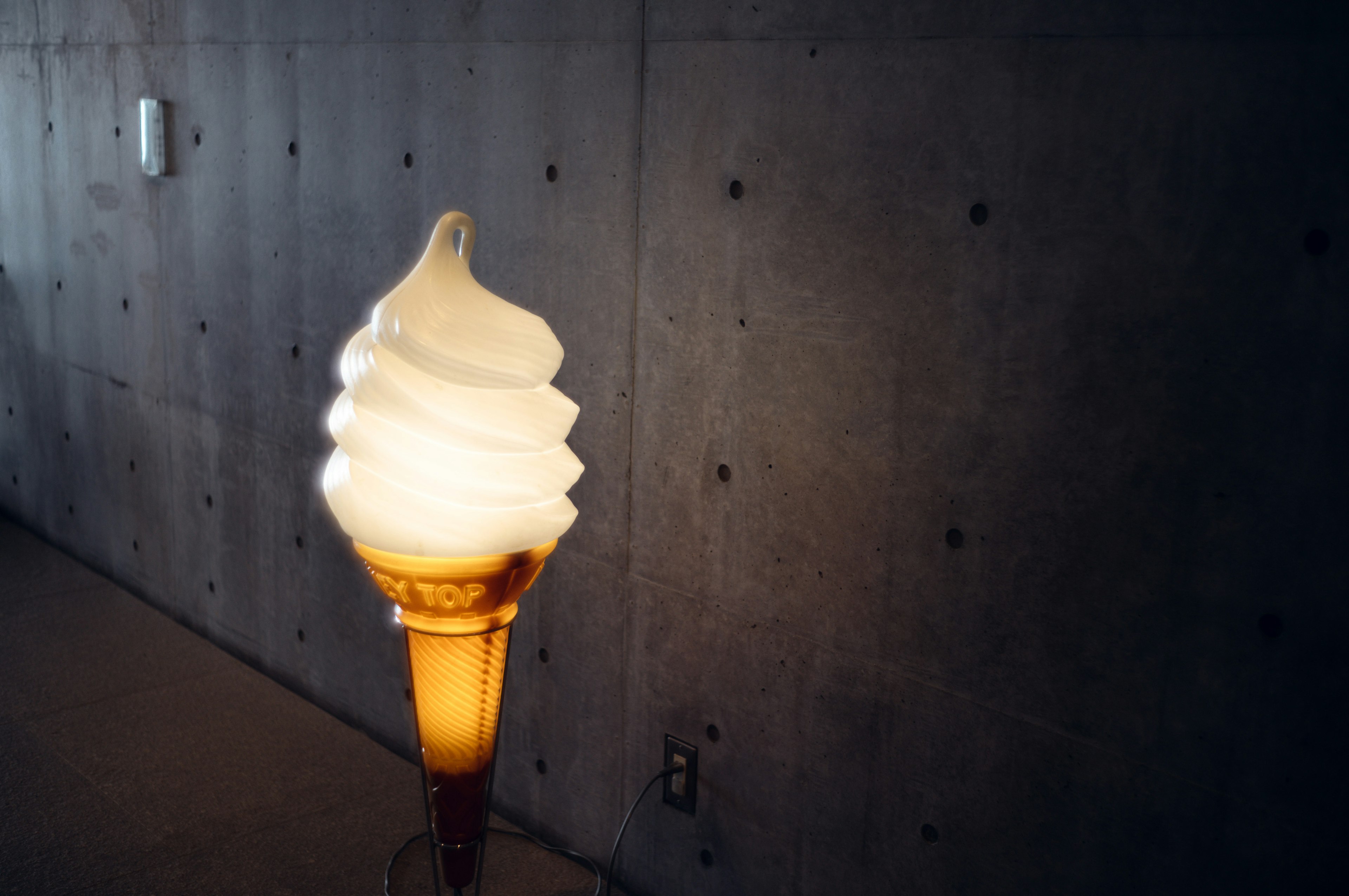 Una lámpara en forma de helado suave está frente a una pared de concreto