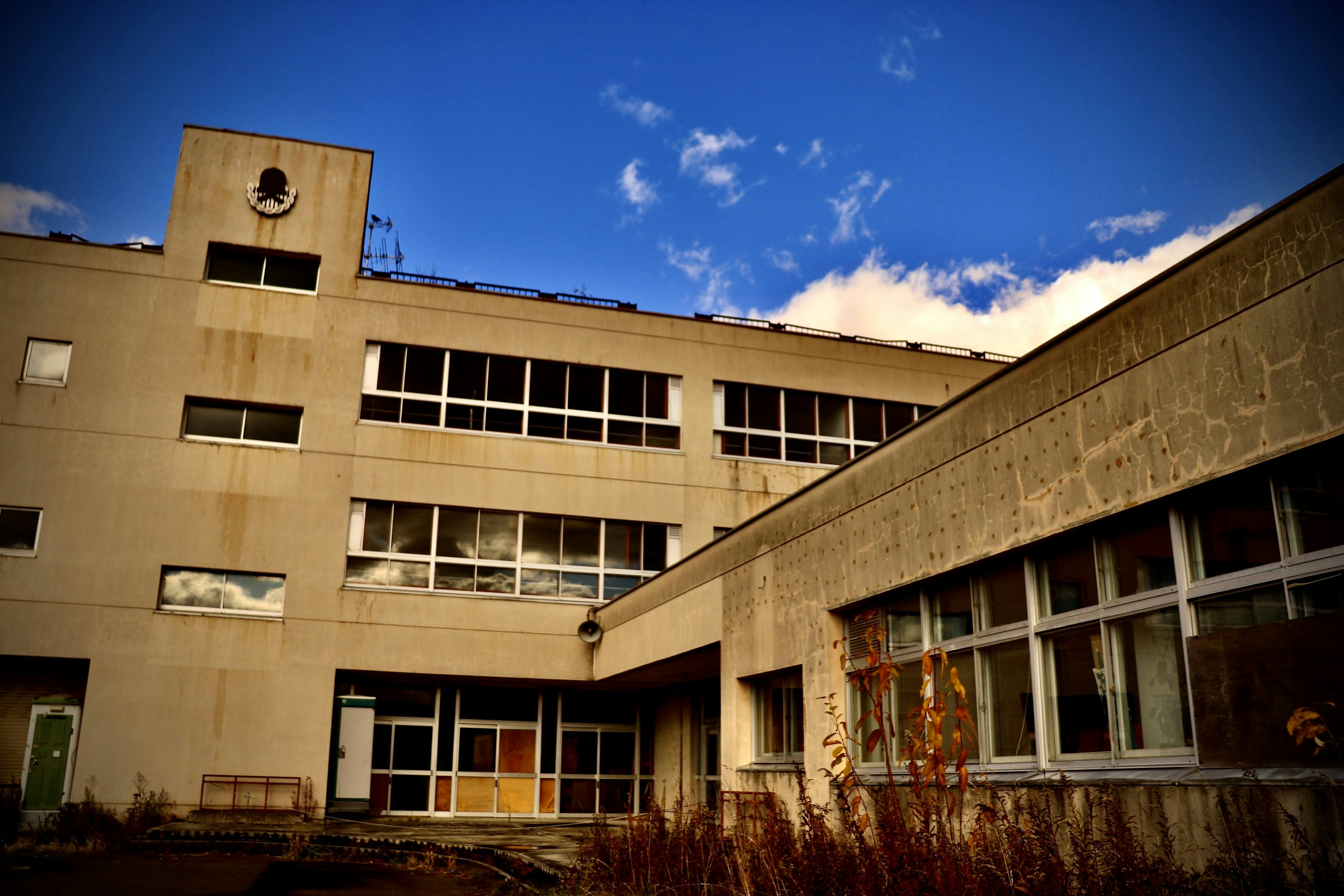 Exterior of an abandoned school building with blue sky and clouds in the background