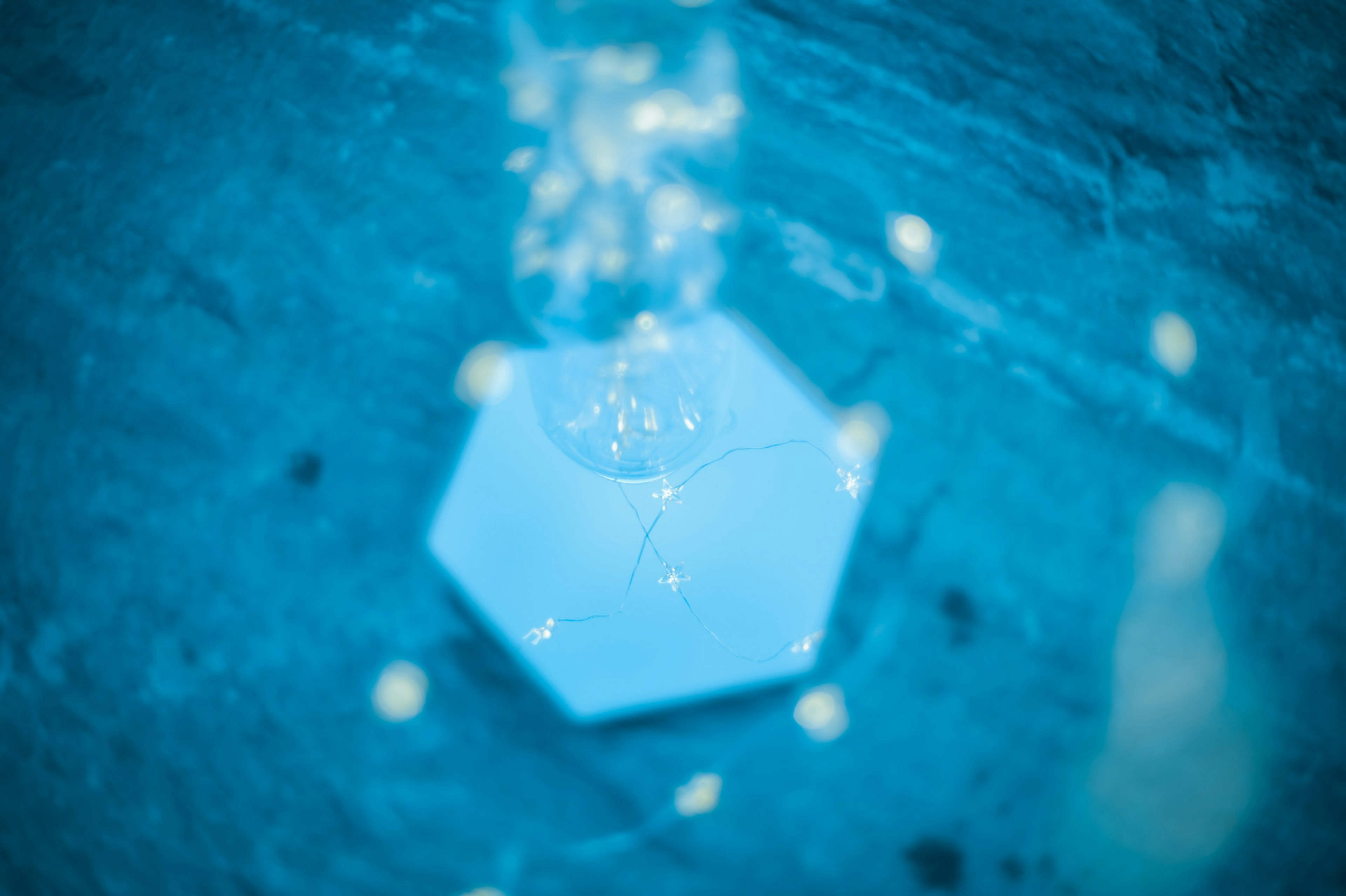 Hexagonal object with reflections on a blue background and scattered light spots