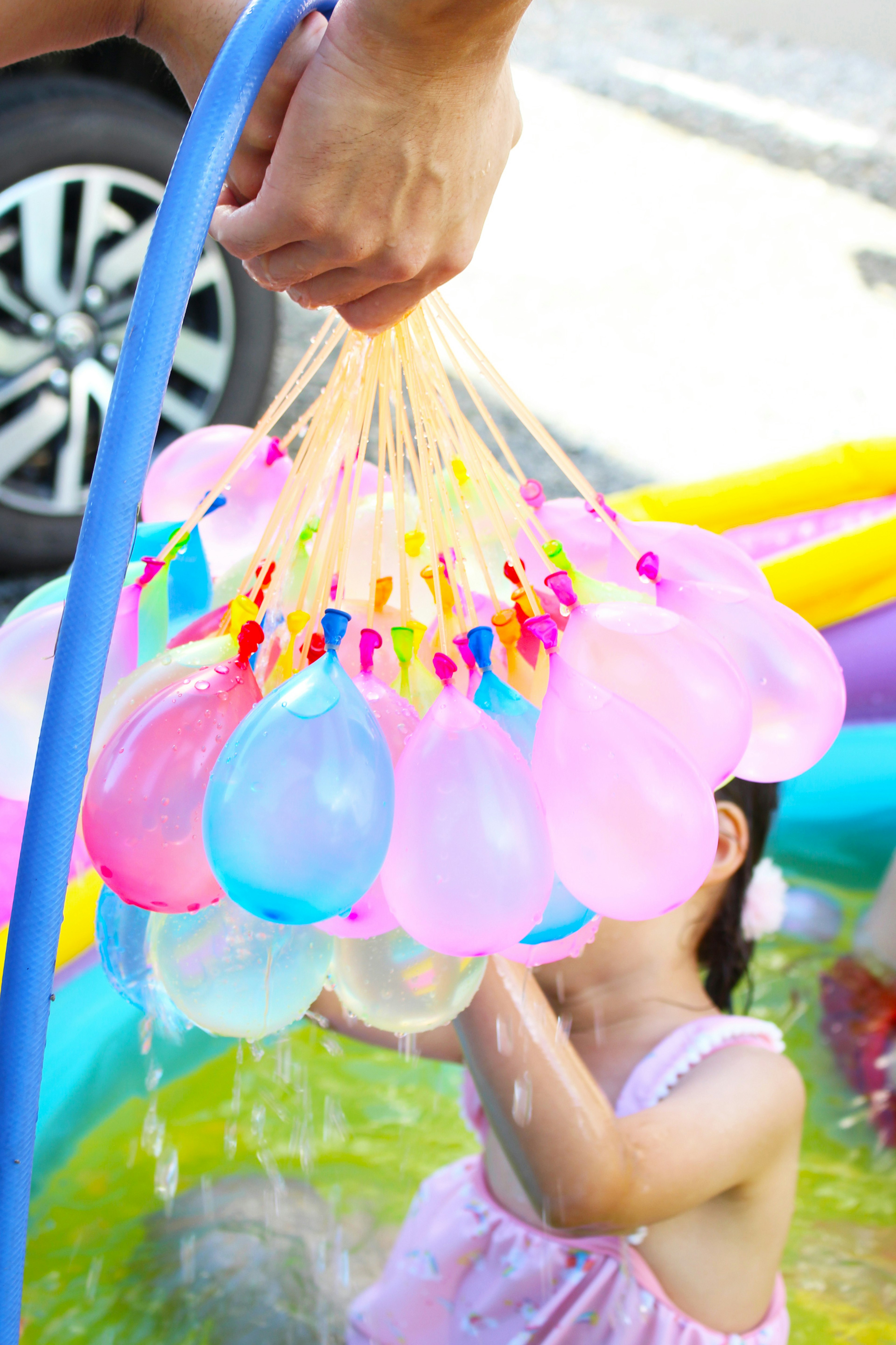 Tangan memegang sekelompok balon air berwarna dengan anak bermain di latar belakang