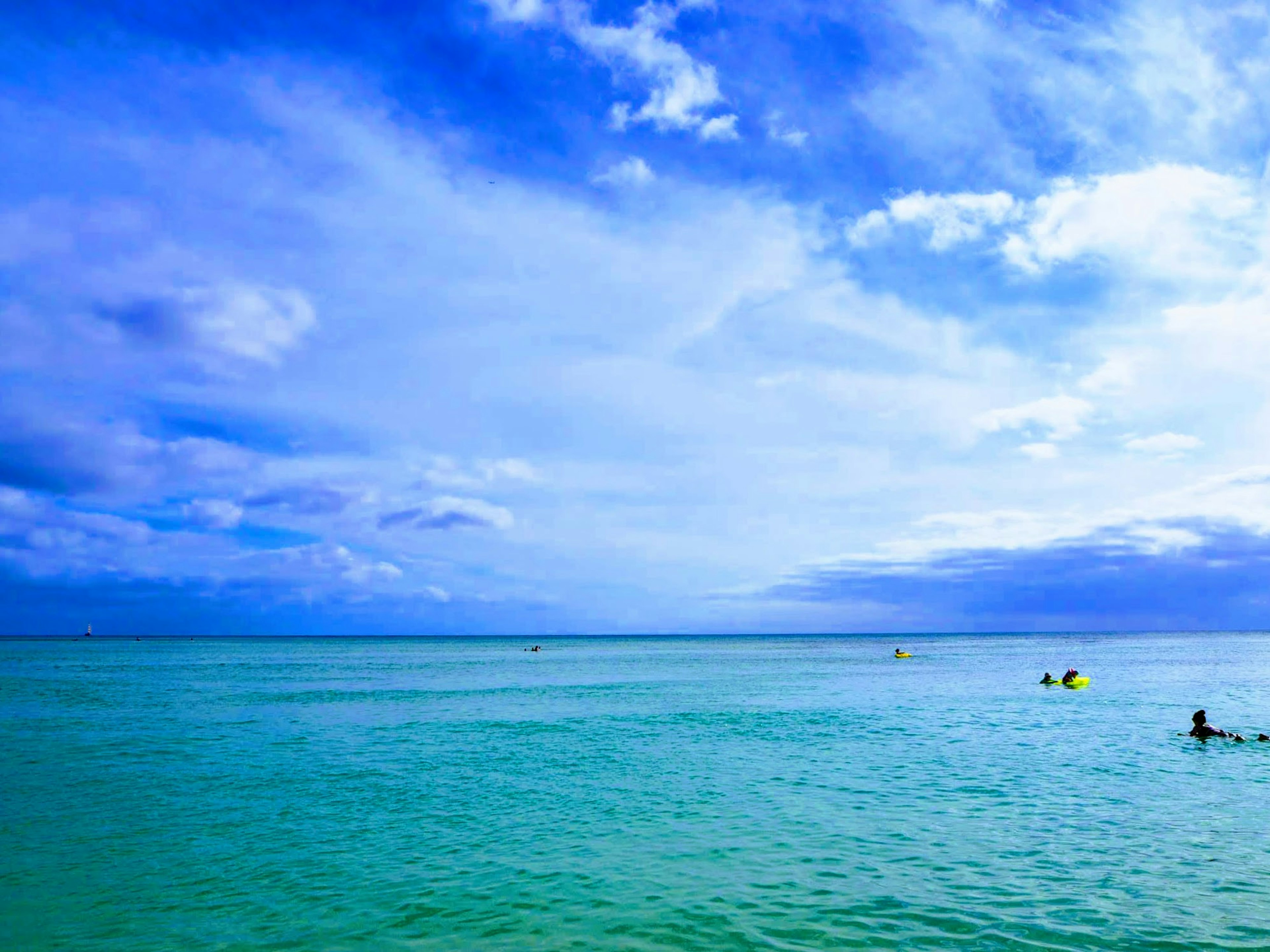 Pemandangan laut biru dan langit dengan orang-orang yang berenang