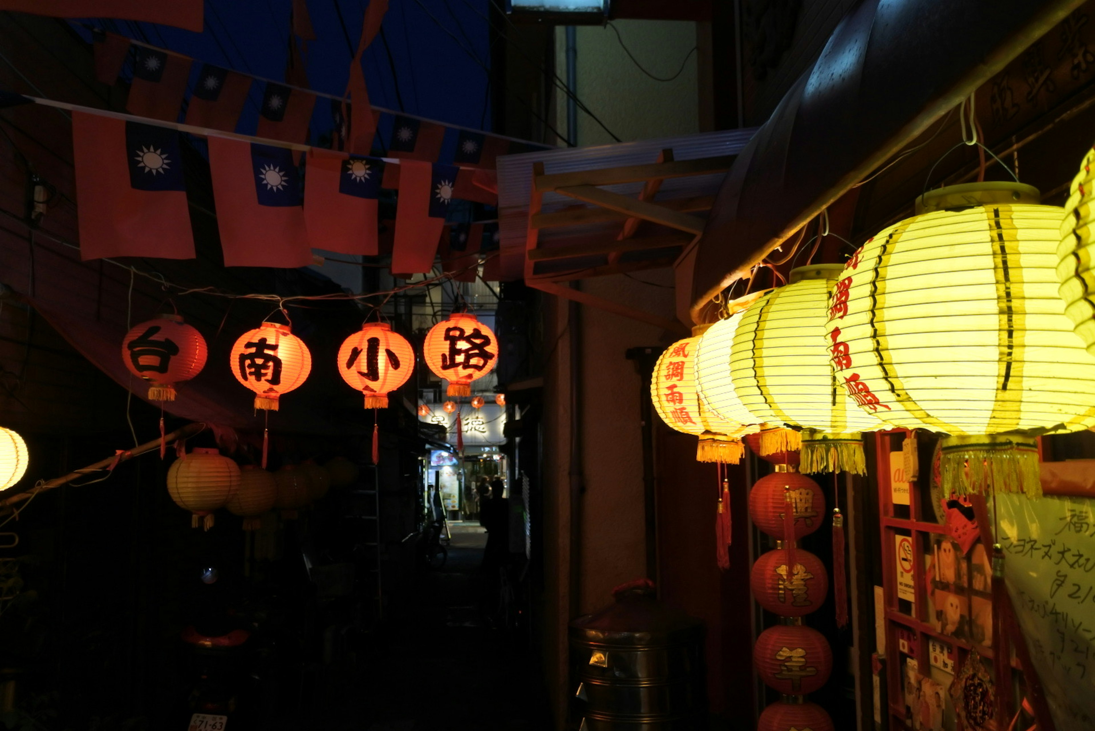 Narrow alleyway illuminated by colorful lanterns and red banners at night