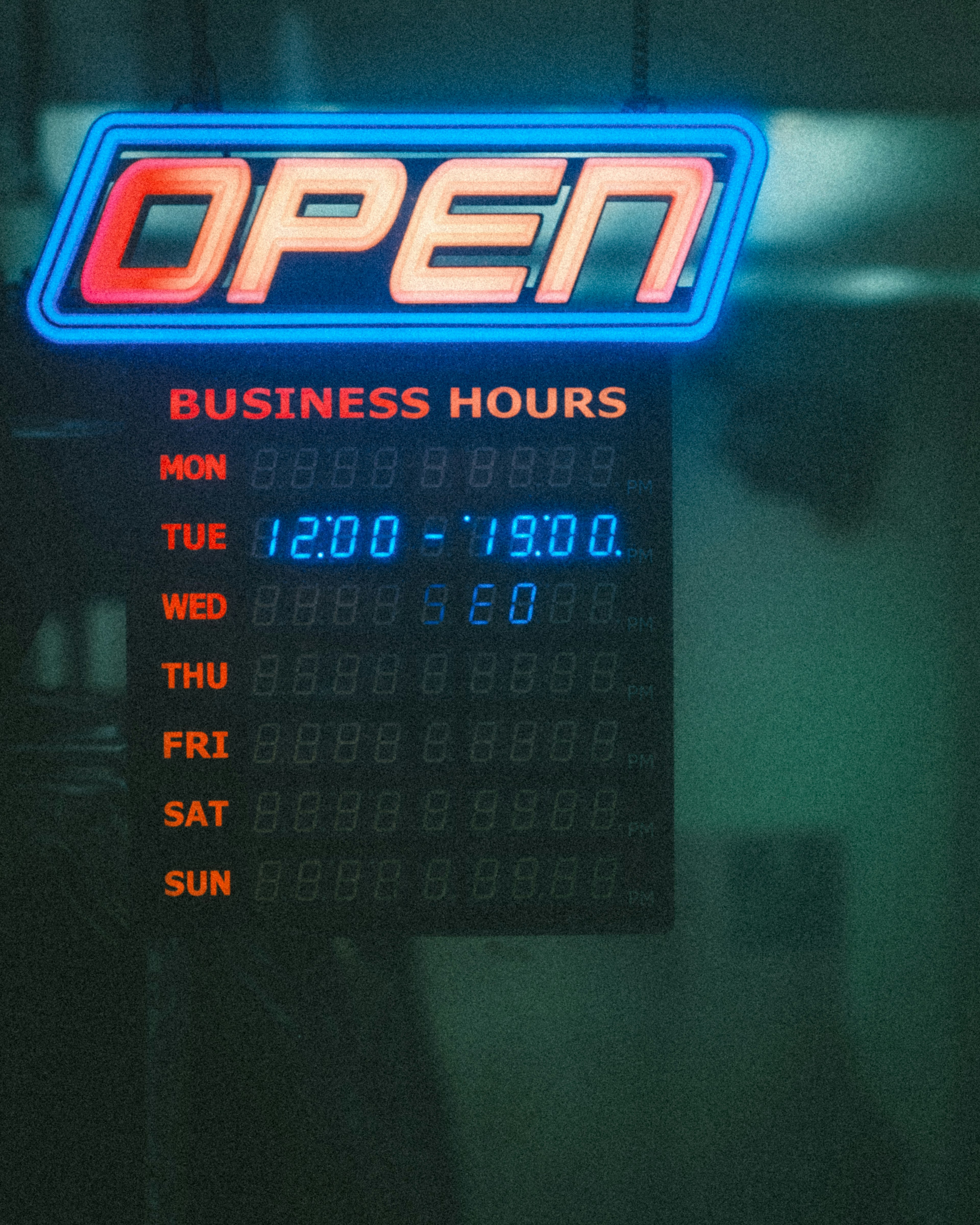 Neon 'OPEN' sign with business hours displayed on a black board