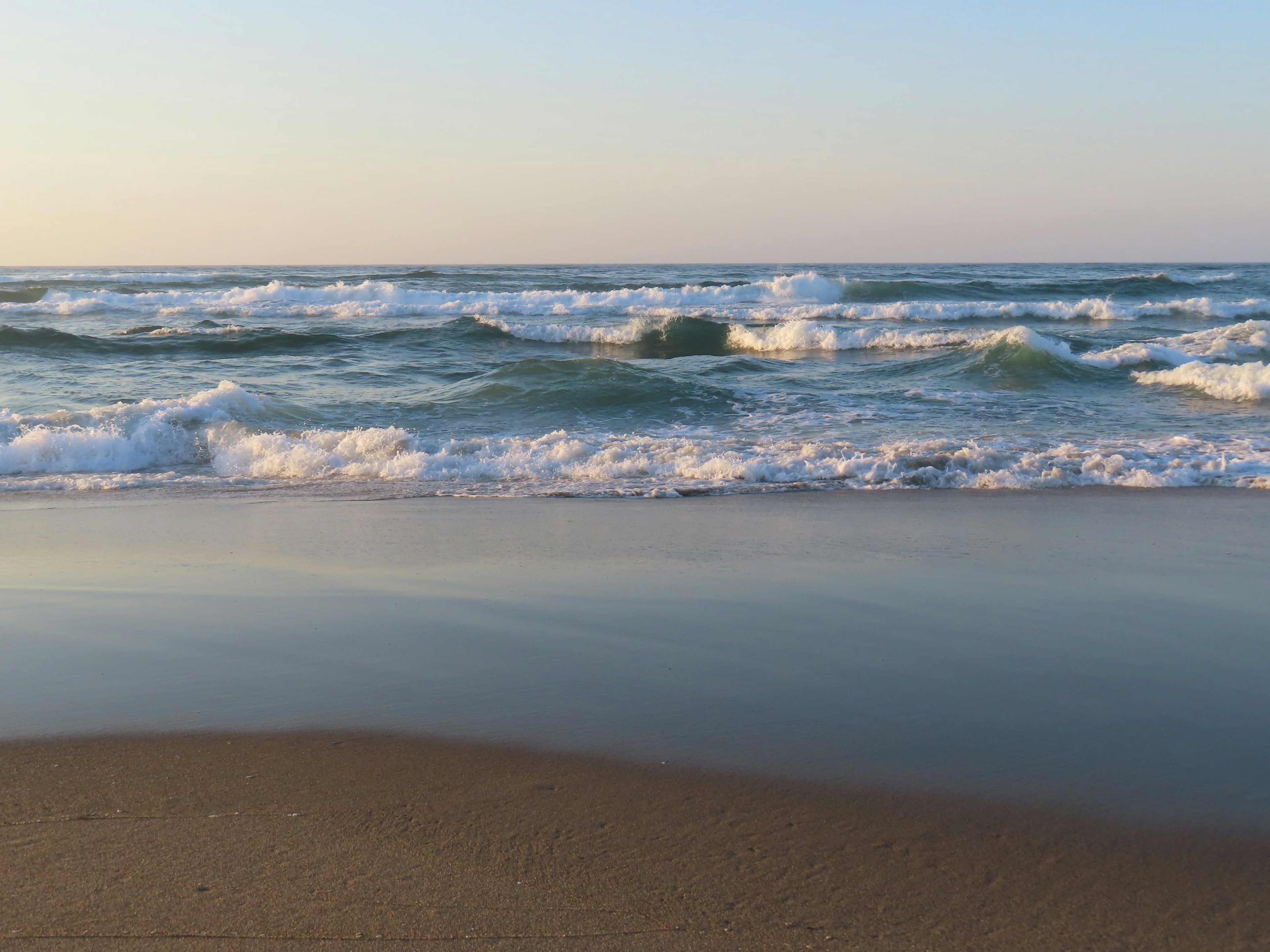 Paesaggio marino con onde e spiaggia sabbiosa che riflette la luce solare